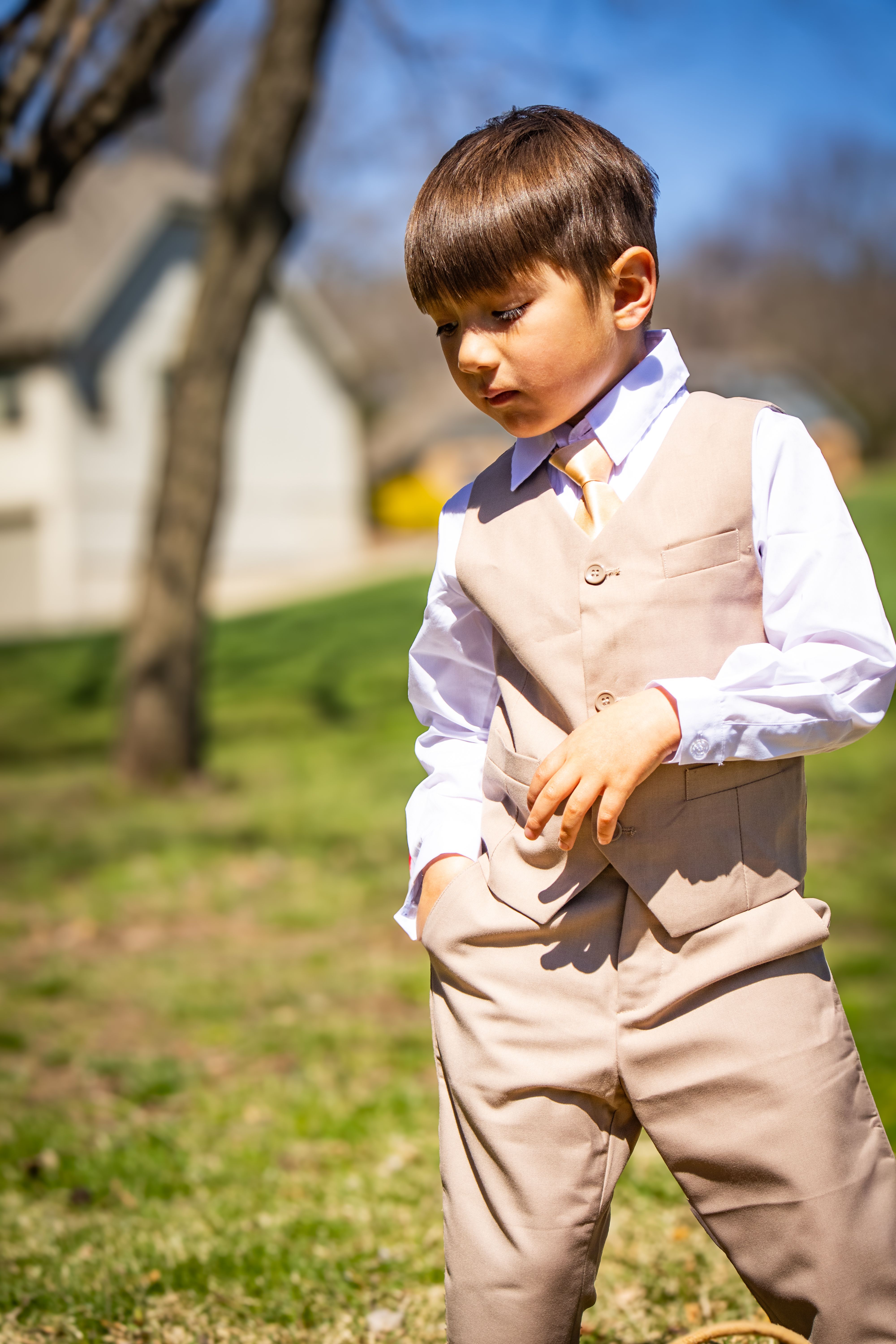 A young boy in a tan vest enjoys a sunny day outdoors, exuding a youthful charm and style.