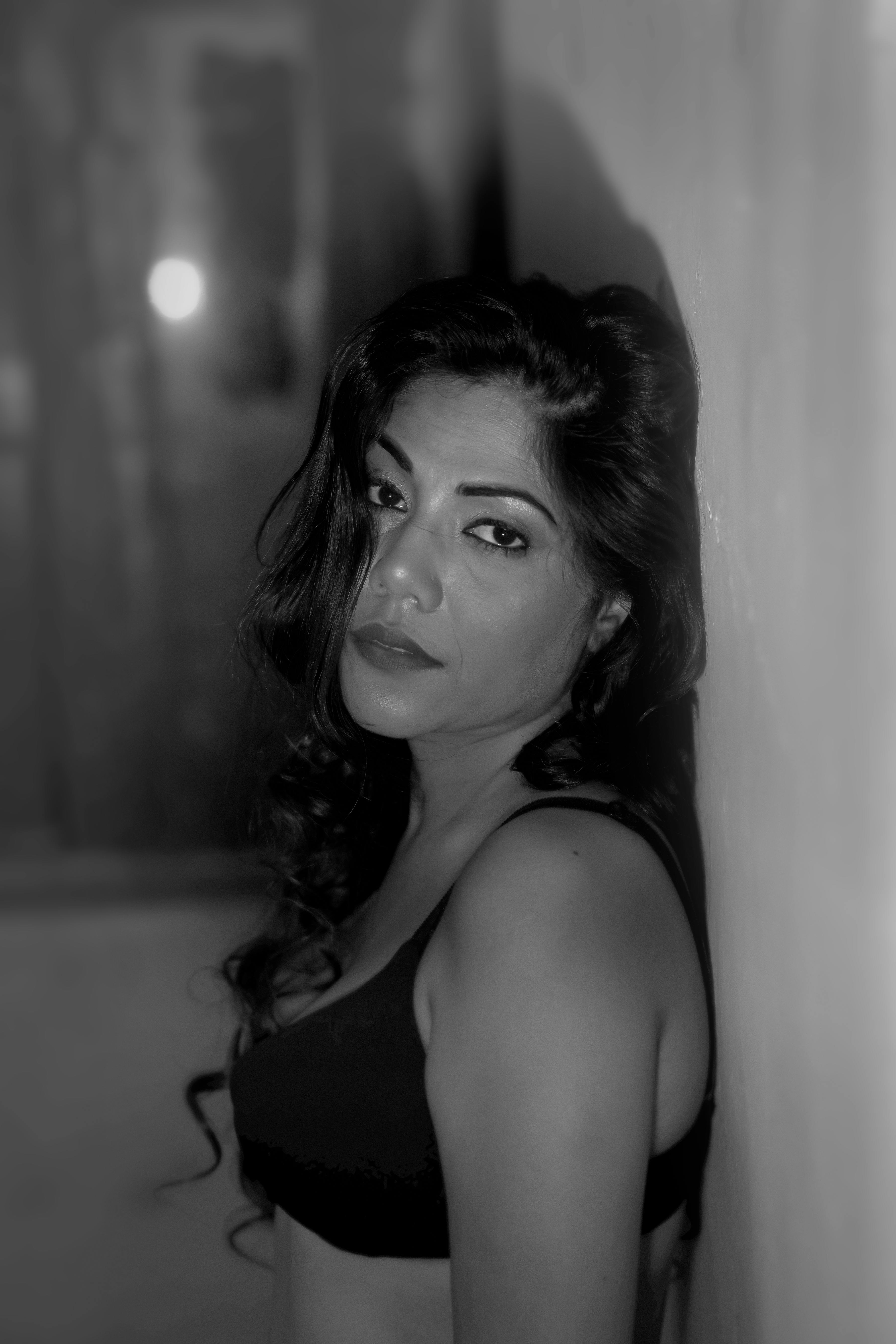 Elegant black and white portrait of an Indian woman leaning against a wall.