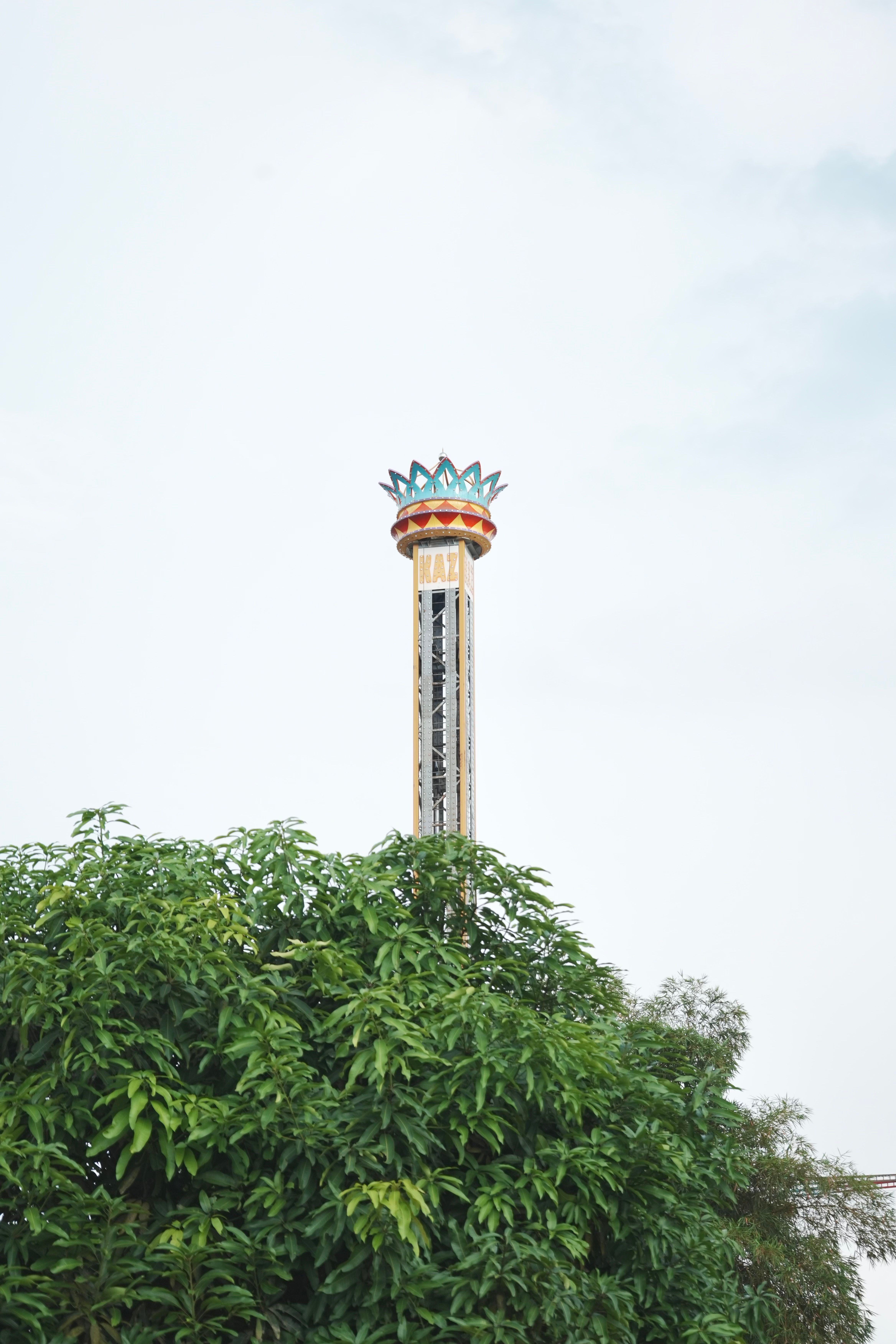 A colorful amusement park ride tower rises above green trees under a clear sky.