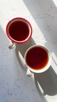 Overhead view of two tea cups casting shadows on a marble surface, with natural light.