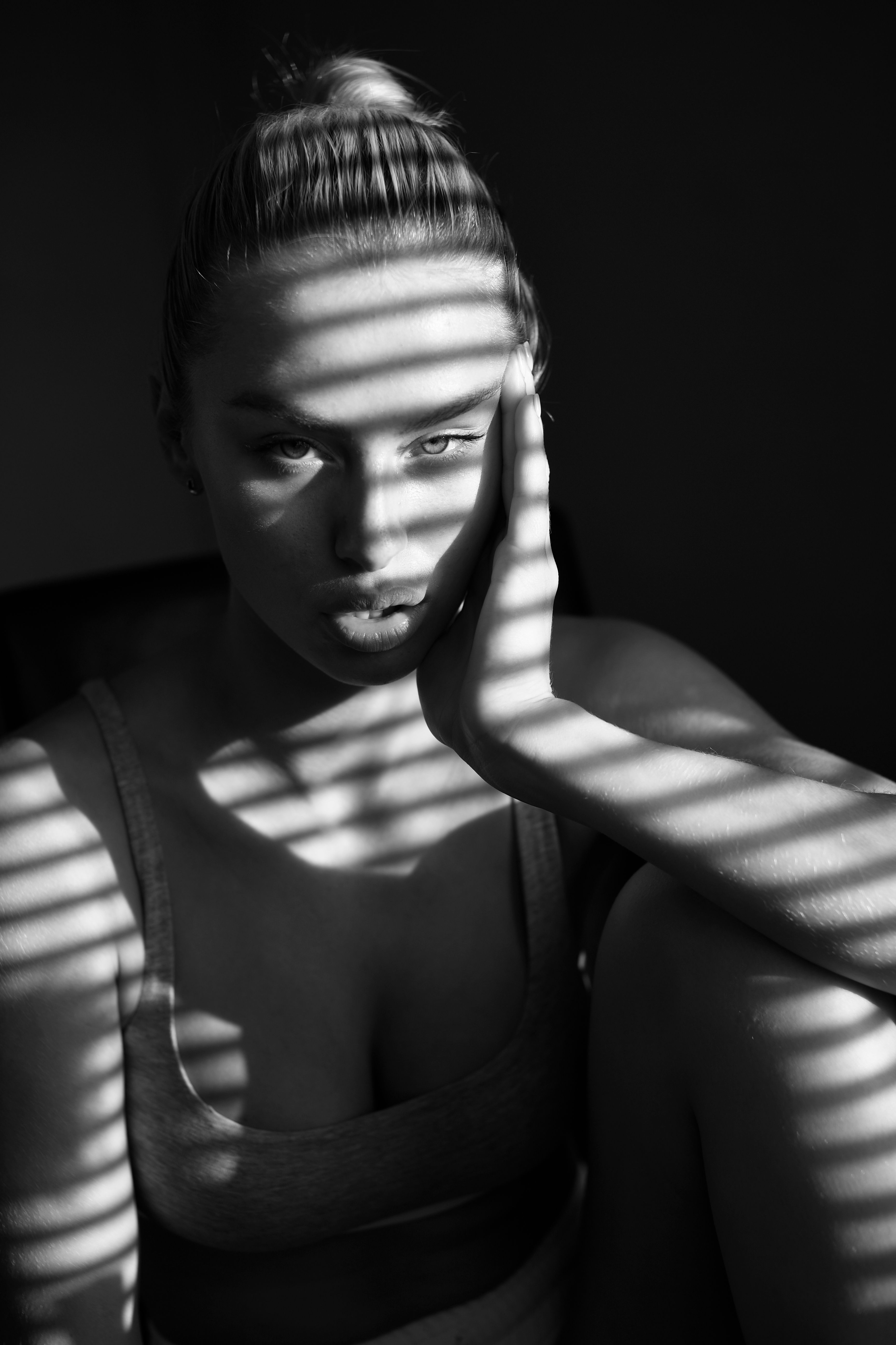 Artistic black and white portrait with dramatic light and shadow play from window blinds.