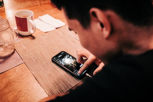 Person uses smartphone while enjoying a drink at a warm-lit wooden table.