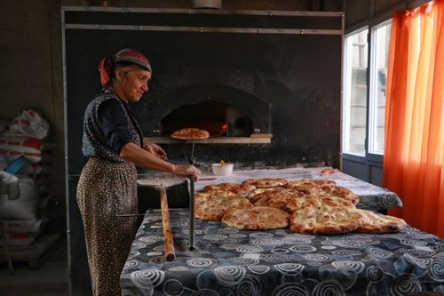 Free A woman baking traditional bread using a wood-fired oven in a cozy, rustic bakery. Natural lighting and warm atmosphere. Stock Photo