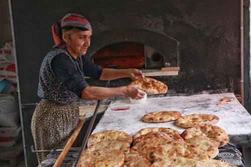Free Elderly woman baking traditional bread in an artisan oven, showcasing cultural heritage. Stock Photo