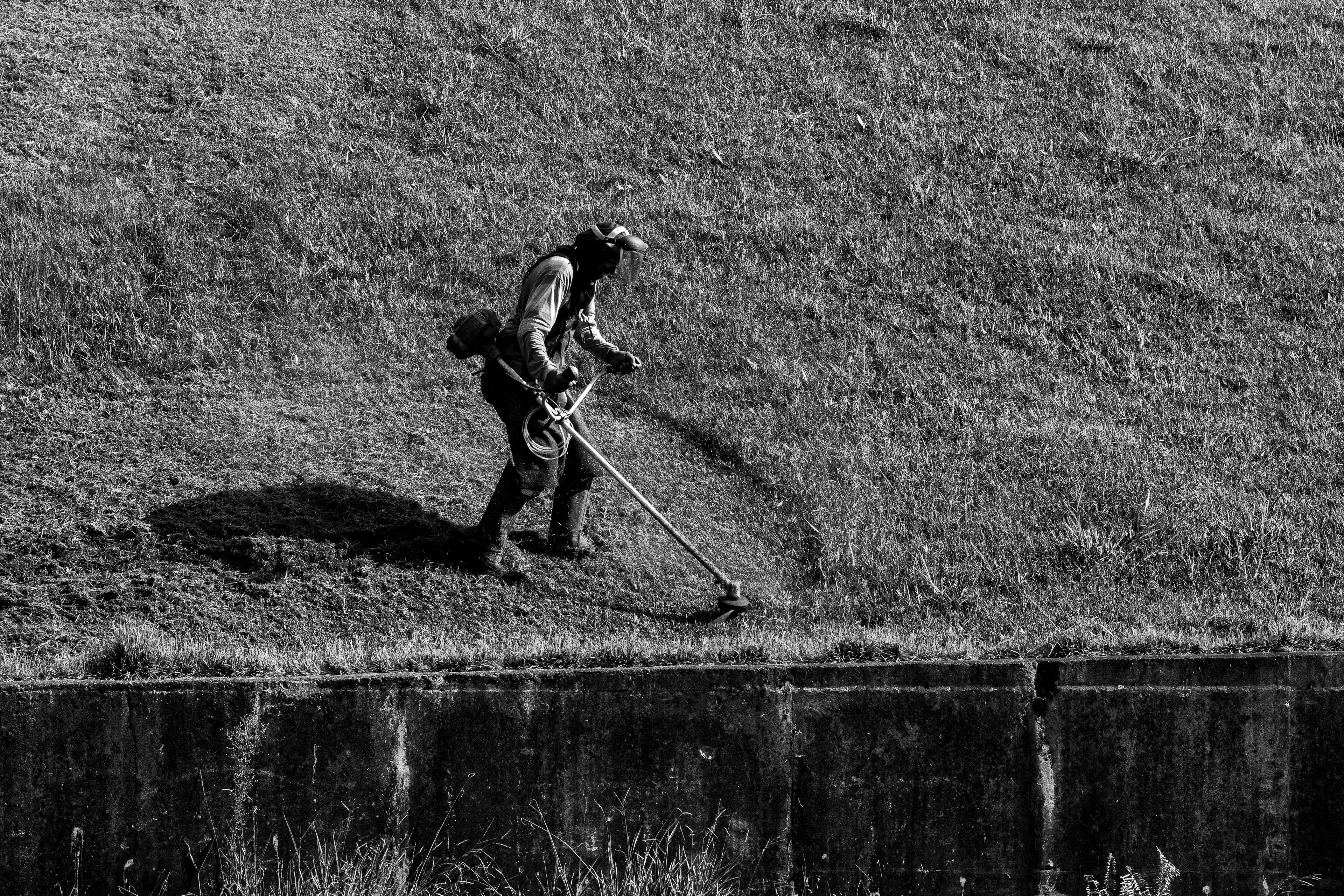 Monochrome image of a person trimming grass on a slope, showcasing outdoor garden maintenance.