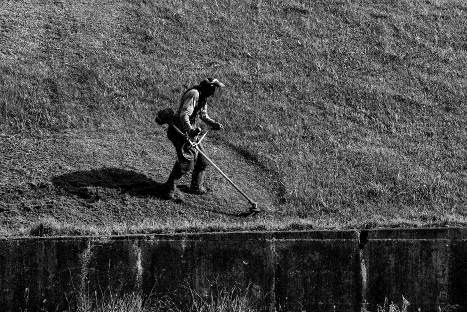Monochrome image of a person trimming grass on a slope, showcasing outdoor garden maintenance.