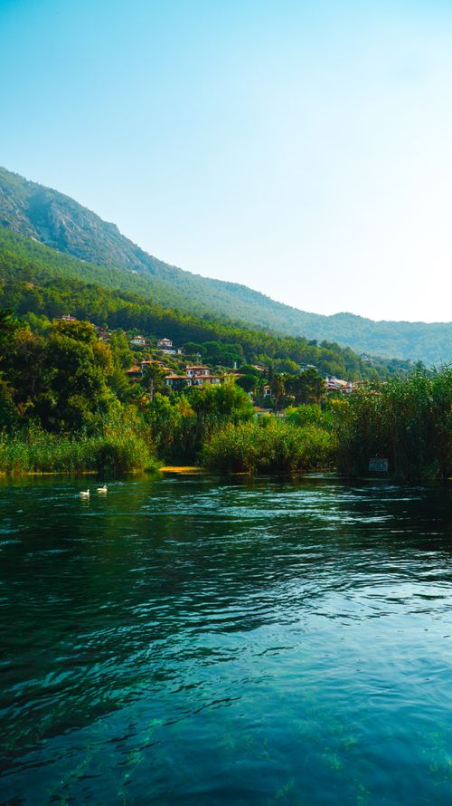 Free Serene river flow amidst lush greenery and distant mountain backdrop. Stock Photo