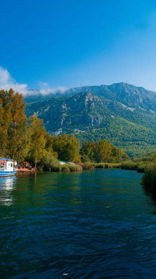 Free A picturesque river scene with a mountain and lush greenery under a clear blue sky. Stock Photo