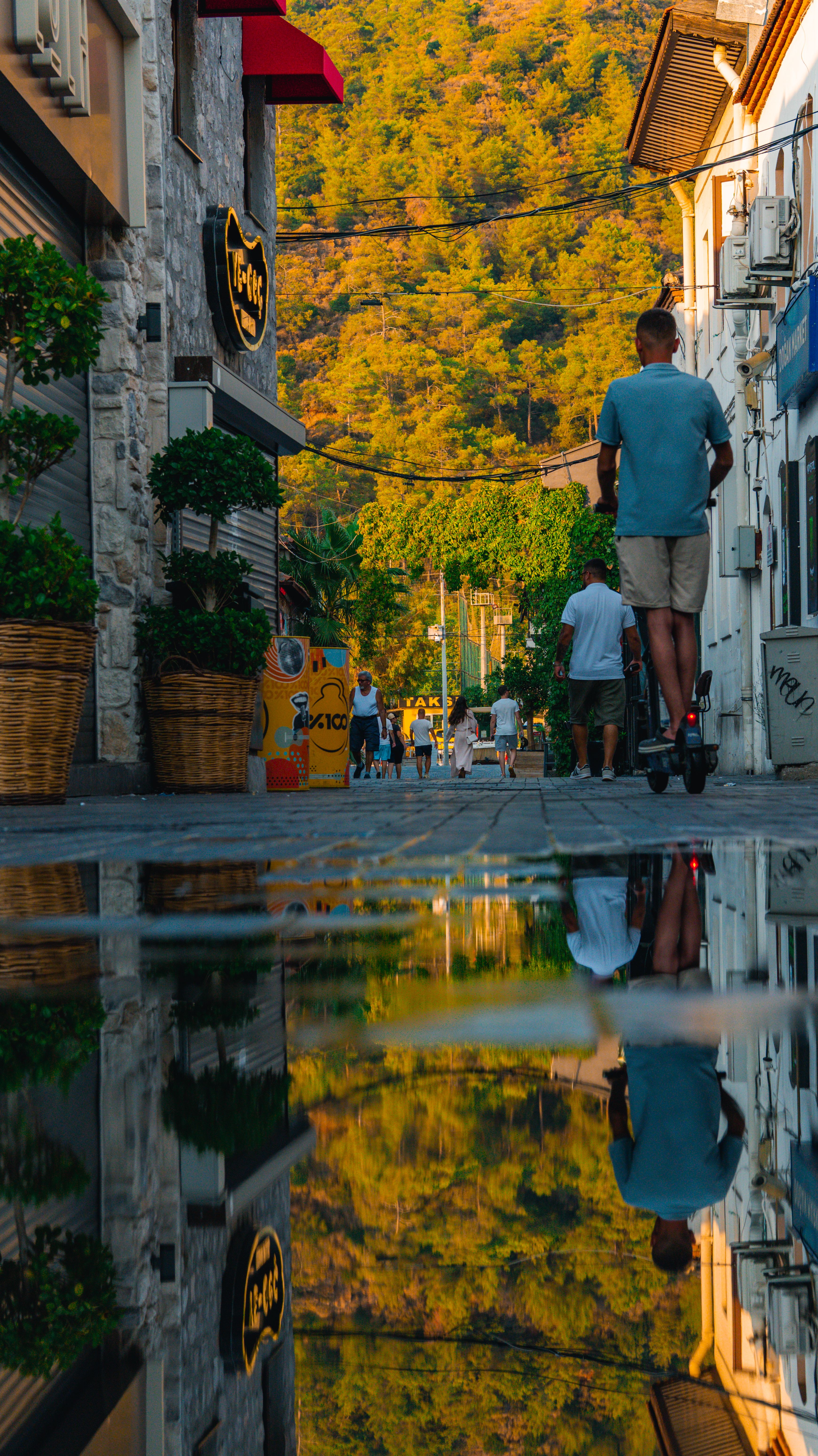 A picturesque street scene with a scooter rider and reflections in a puddle at sunset.