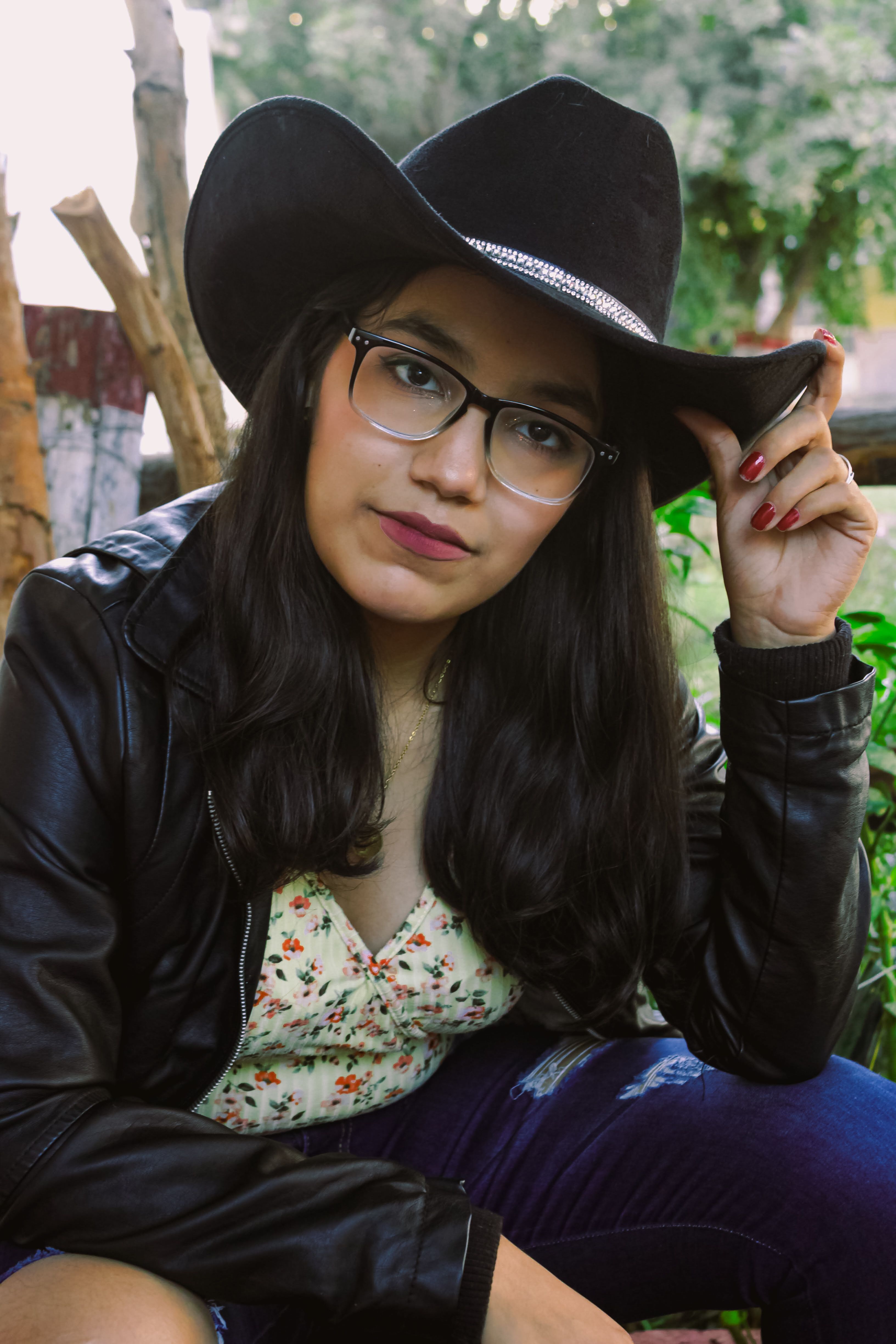 Young woman in a cowboy hat and leather jacket posing outdoors.