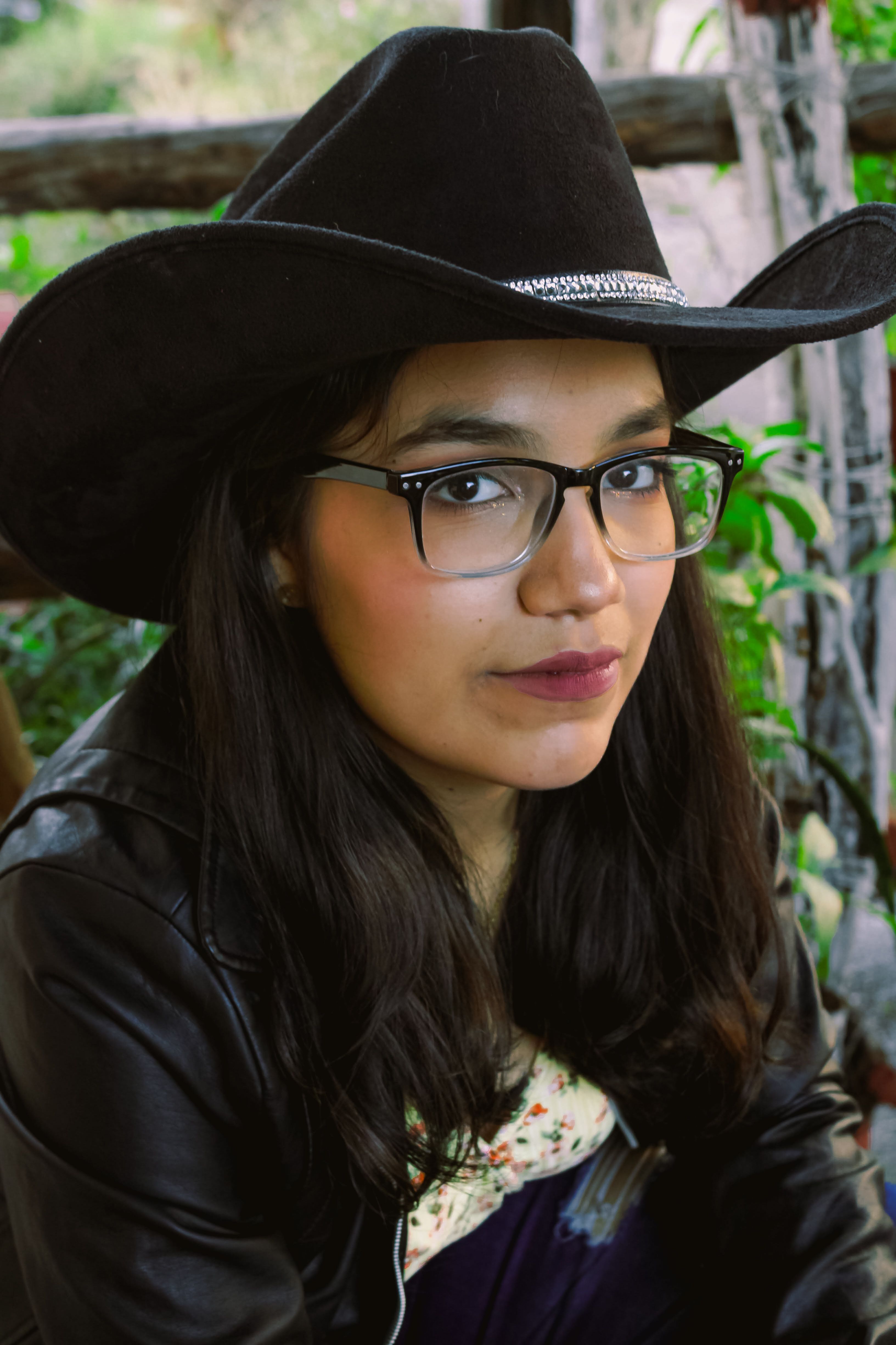 Woman wearing a cowboy hat and glasses in an outdoor setting.