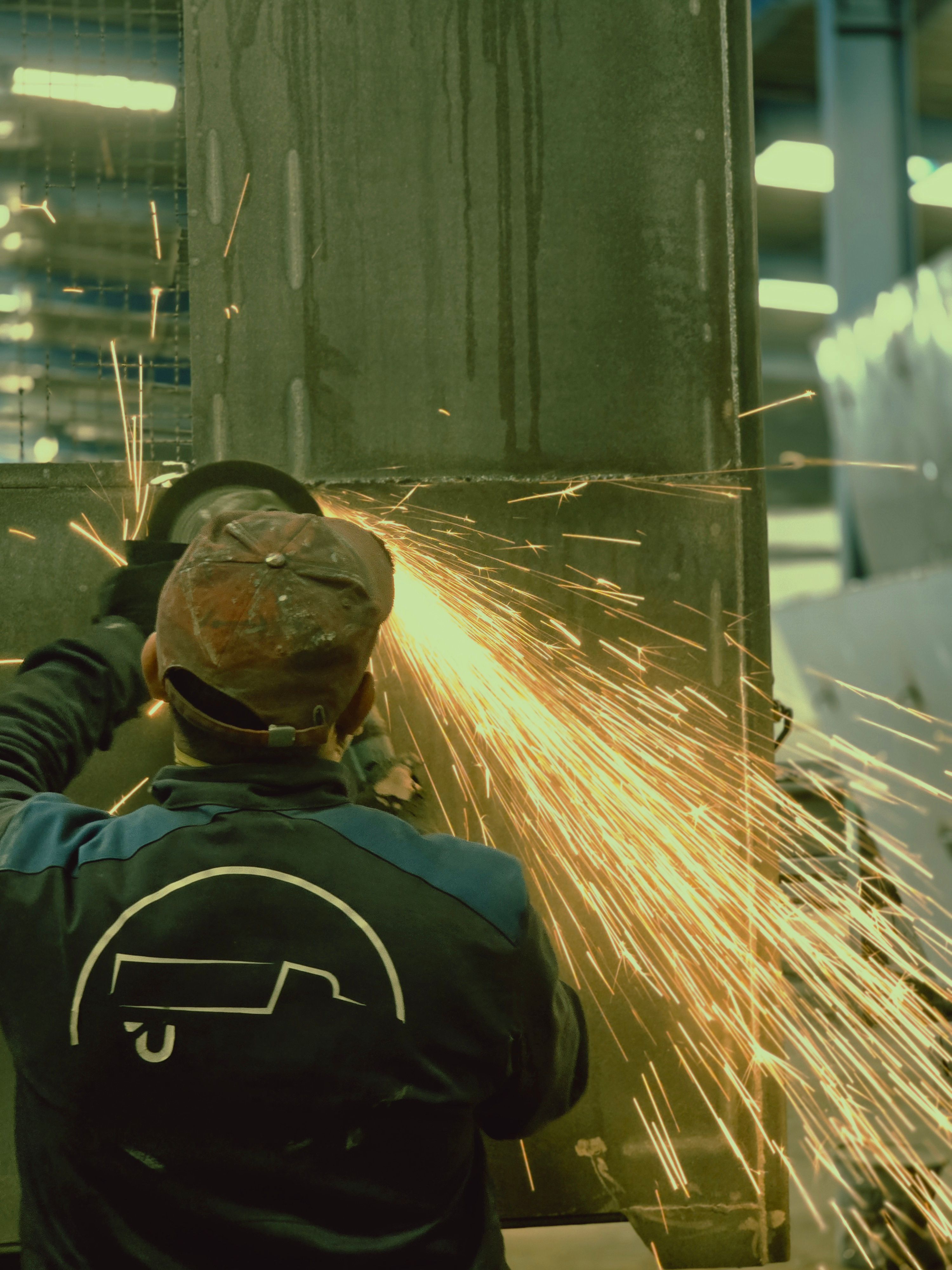 A worker uses an angle grinder on metal, producing vibrant sparks indoors.