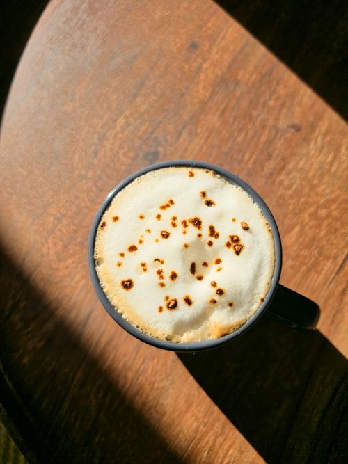 Free Overhead shot of cappuccino with frothy milk art on a wooden table, bathed in sunlight. Stock Photo