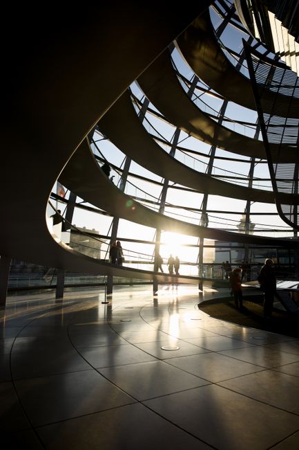 Fotomural Vista de la silueta del interior de la cúpula del Reichstag en Berlín durante la puesta de sol, con gente admirando la arquitectura.