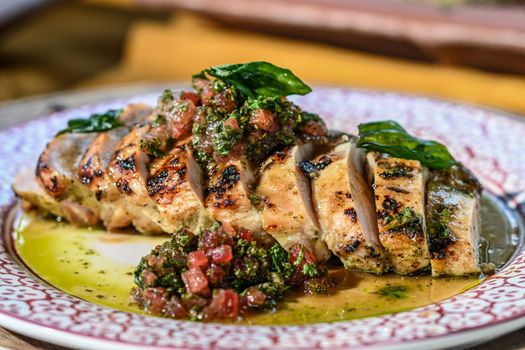 Sliced grilled chicken topped with fresh herb chimichurri sauce on a decorative plate.