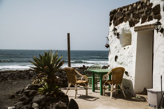 Serene Lanzarote seaside view with rustic cottage and chairs by the ocean.