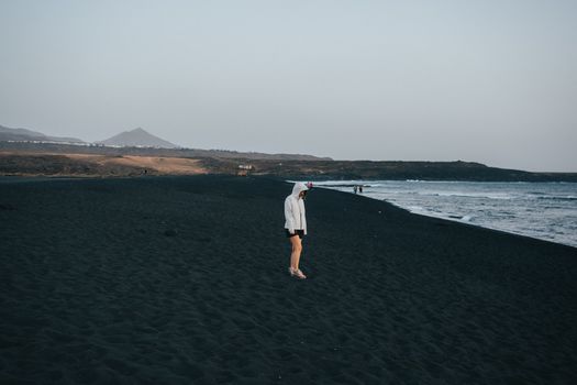 A person stands on the black sand beach of Lanzarote at dusk, highlighting serene coastal solitude.. pexels, person, stands