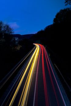Captivating long exposure of colorful light trails on a highway at night, under a clear blue sky.