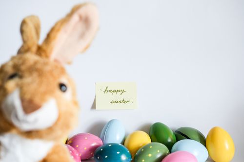 Free A charming Easter setup with a plush bunny, colorful eggs, and 'happy easter' note. Stock Photo