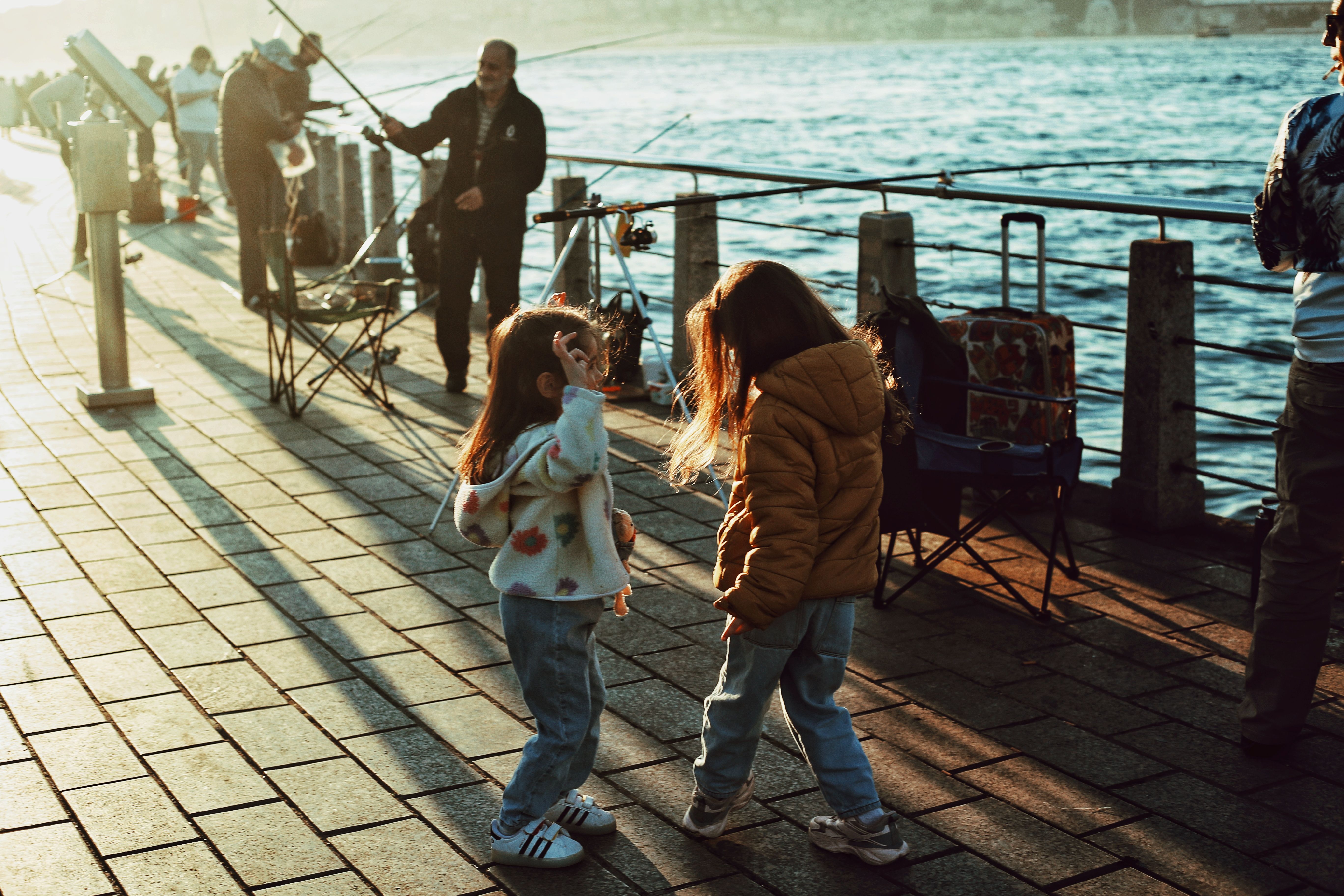 Two children play by the Bosphorus in Istanbul at sunset, with fishermen nearby.