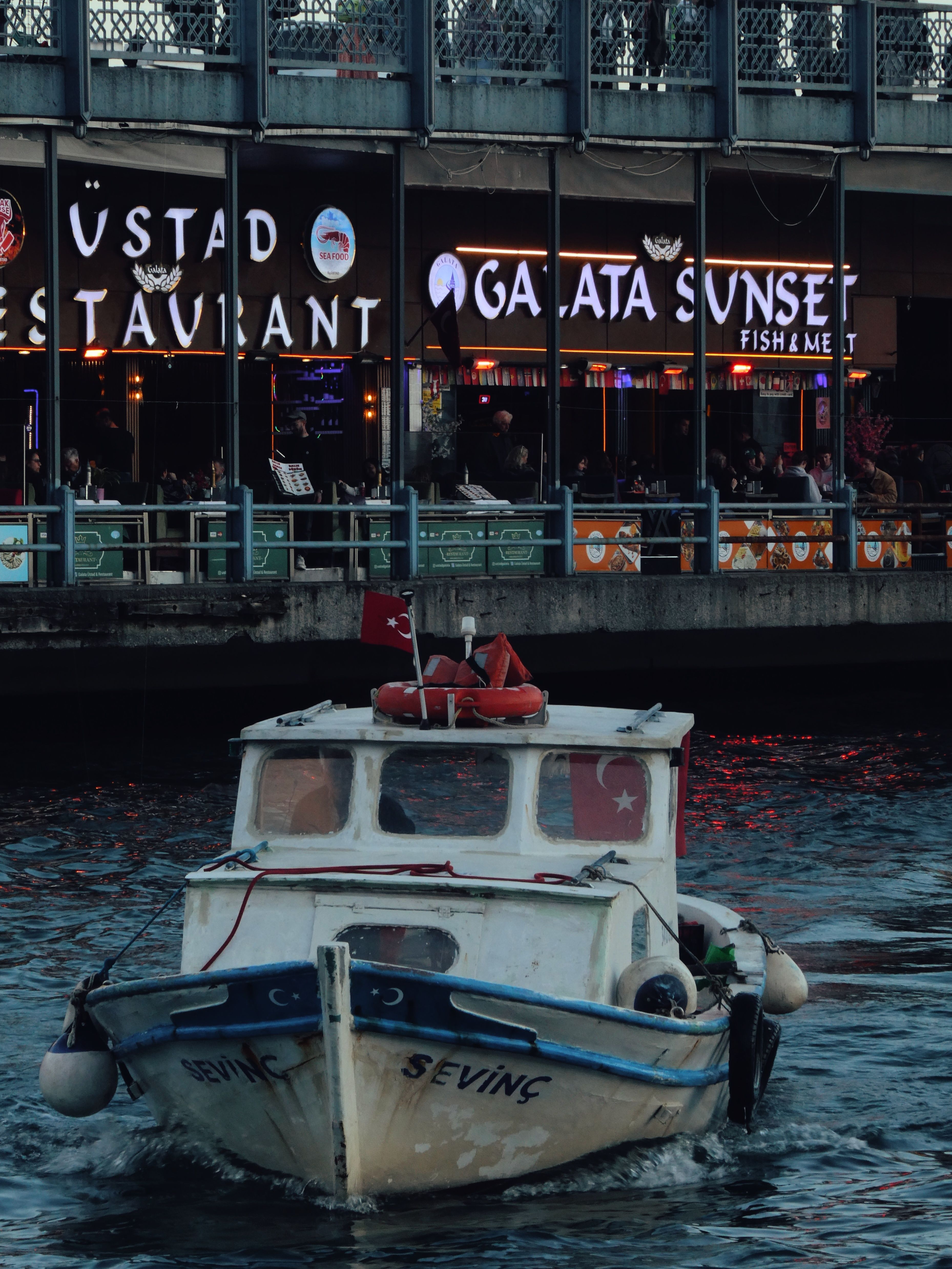A small boat sails near Galata Bridge in İstanbul, showcasing the vibrant nightlife.