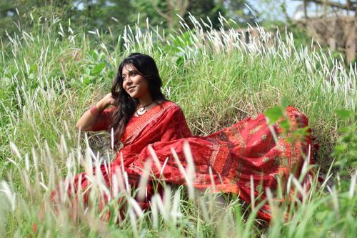 Free A woman in a vibrant red saree enjoys a peaceful moment in a lush green field during daylight. Stock Photo