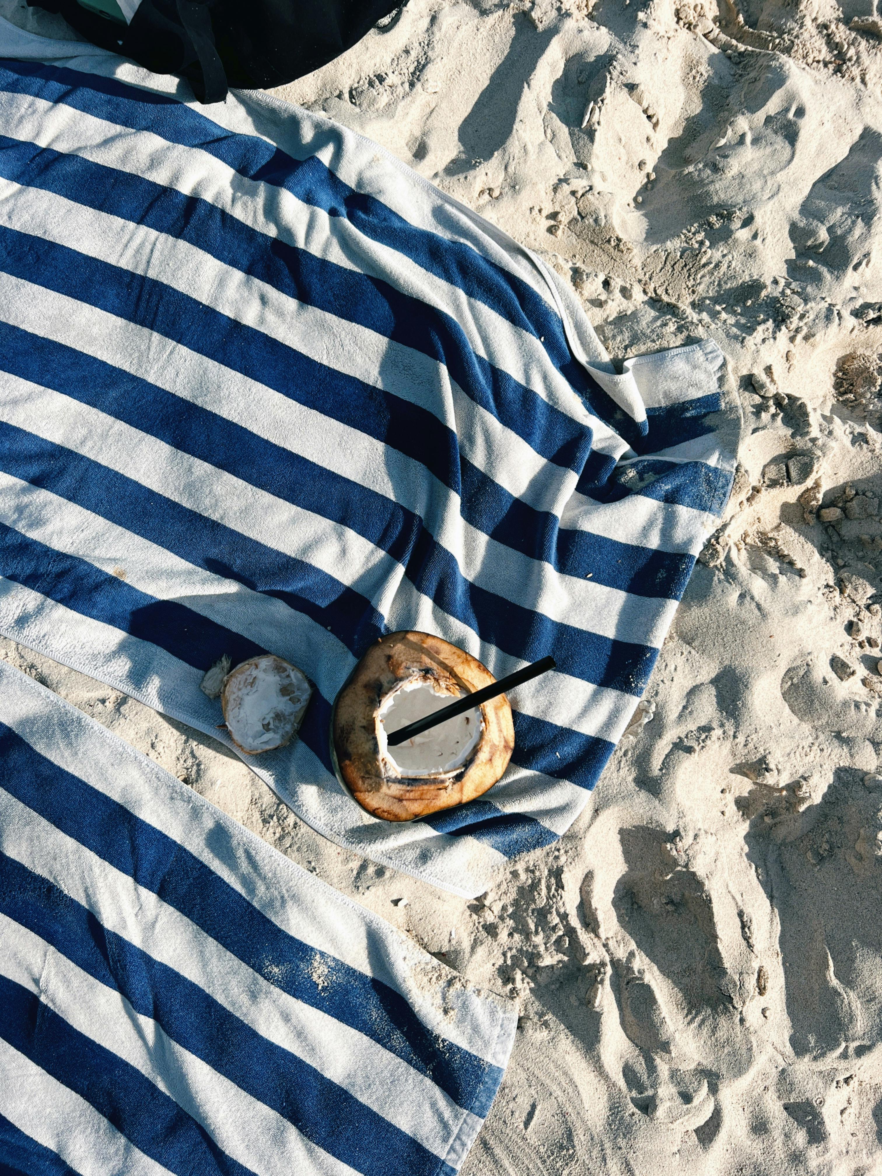 A striped towel on a sandy beach with a fresh coconut drink in the sunlight, perfect tropical vibe.