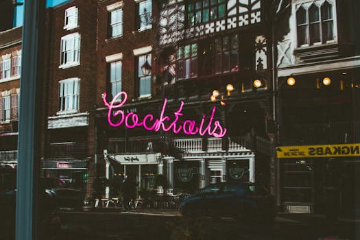 粉红色的霓虹鸡尾酒标志倒映在夜间城市建筑的窗户上