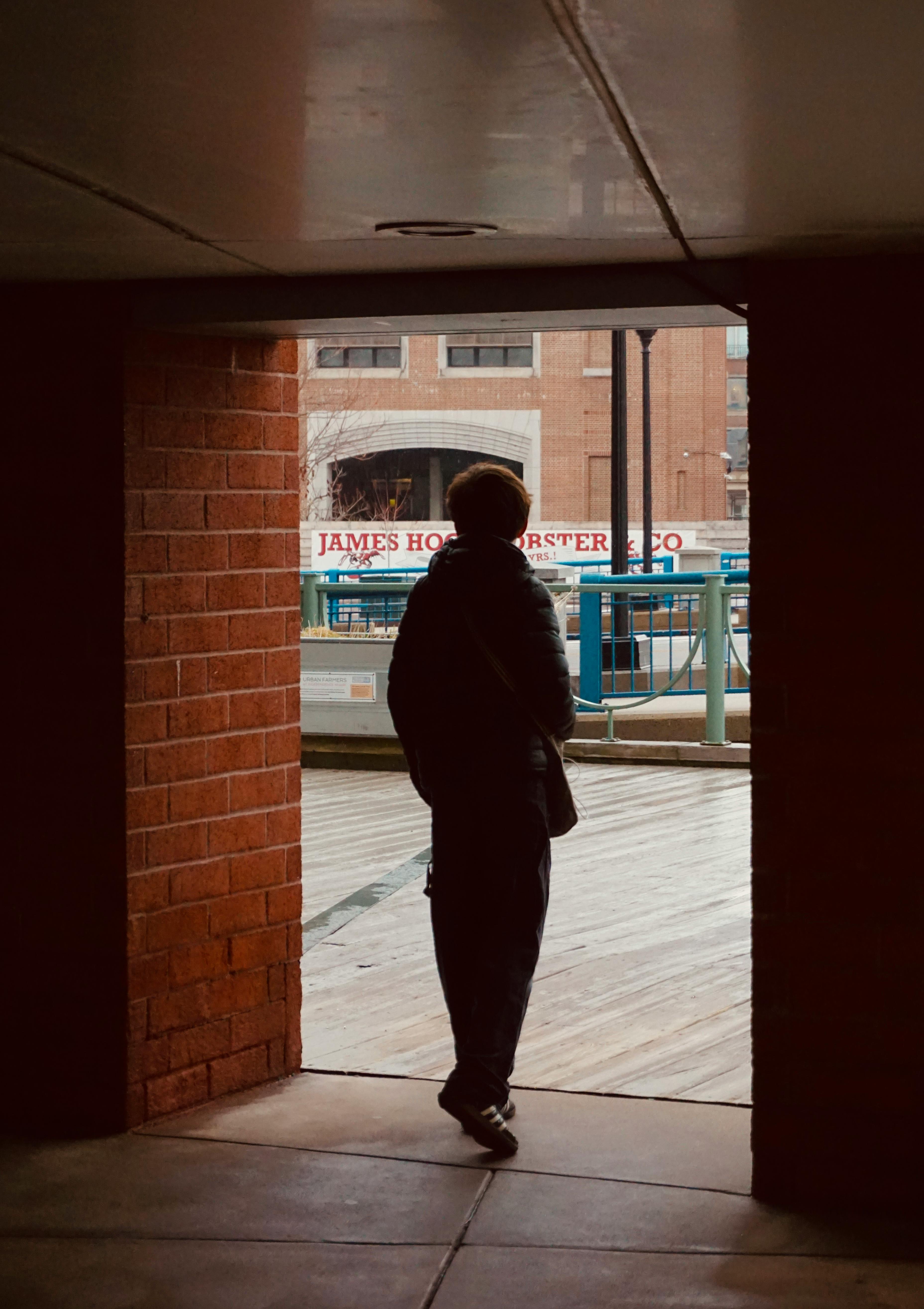 A silhouette of a person standing in an urban alleyway, framed by brick walls.
