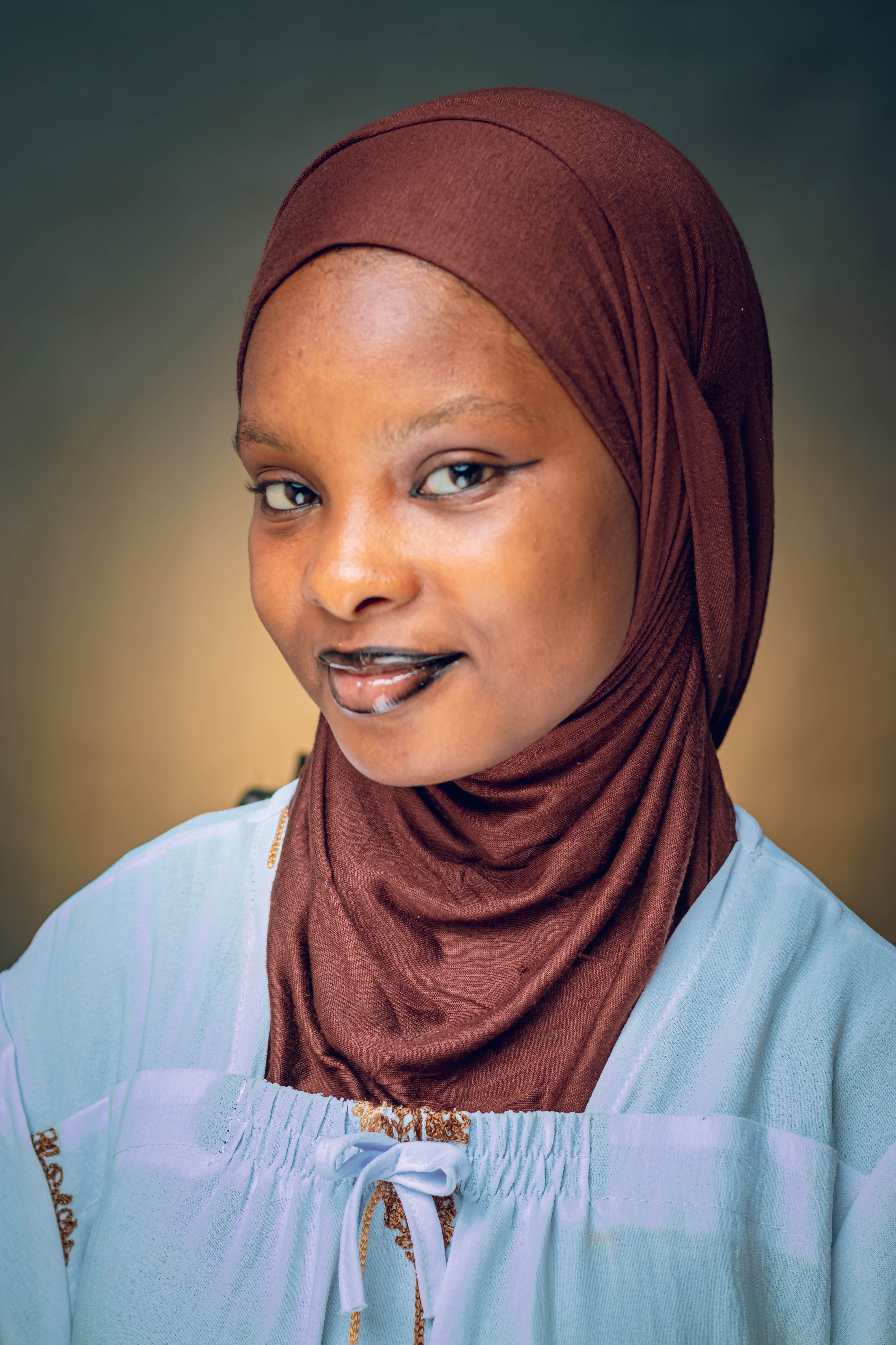 Close-up portrait of a smiling woman wearing a hijab, with a neutral background.