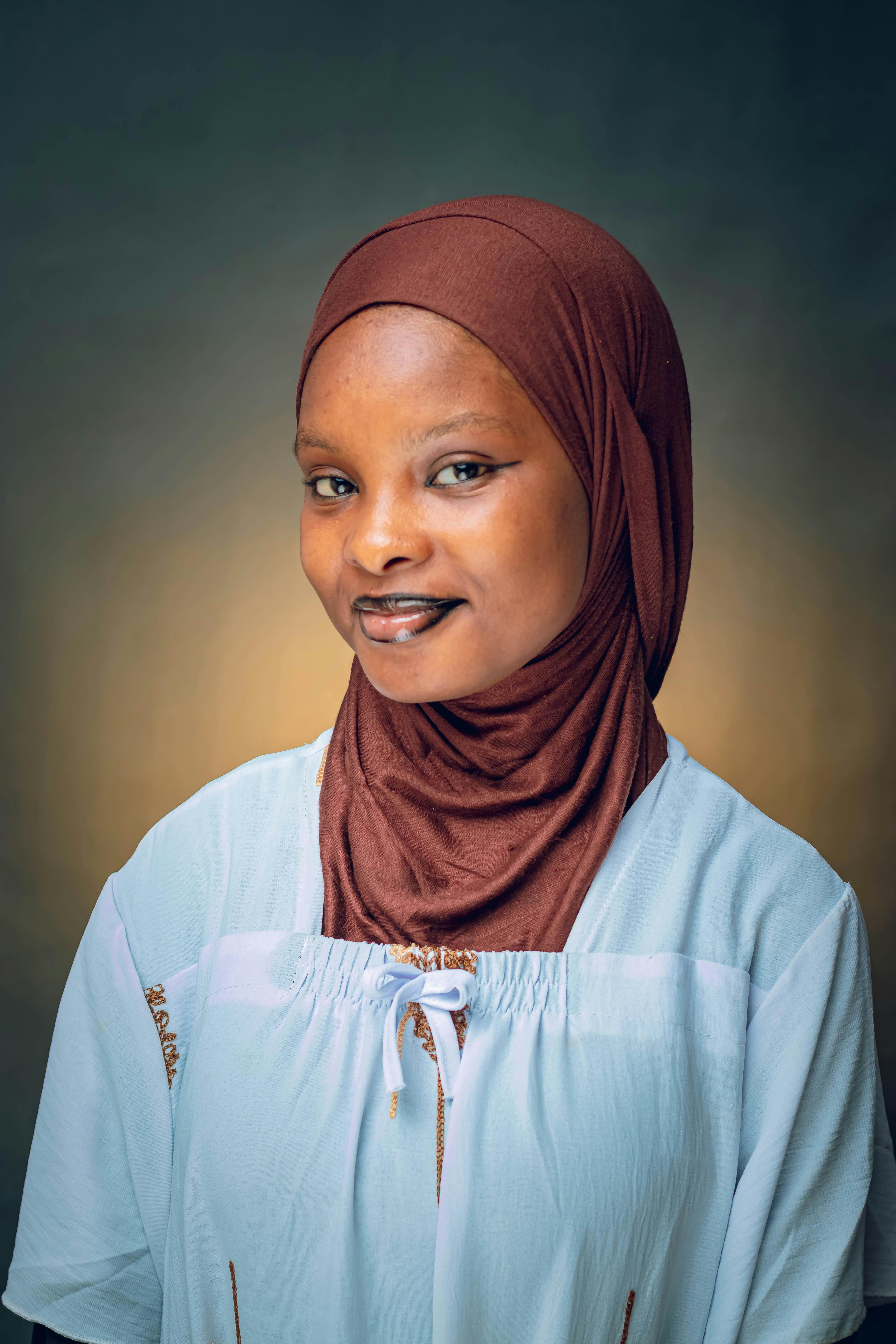 Smiling young woman wearing a hijab against a soft, warm background.