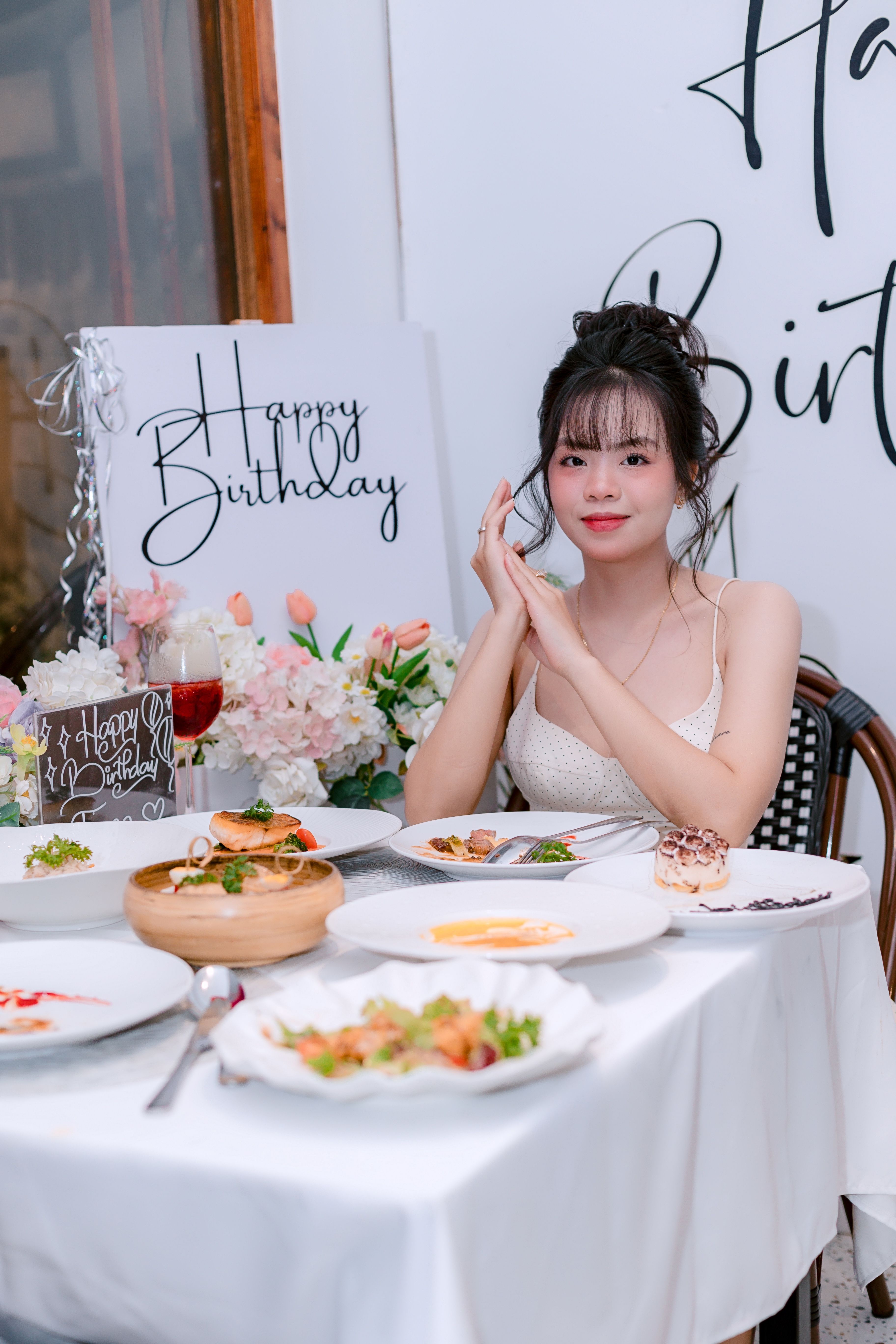 Woman celebrating birthday with elegant dining setup, surrounded by flowers and decor.