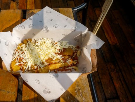A delicious serving of cheesy fries topped with Bolognese sauce, captured outdoors on a rustic wooden table.