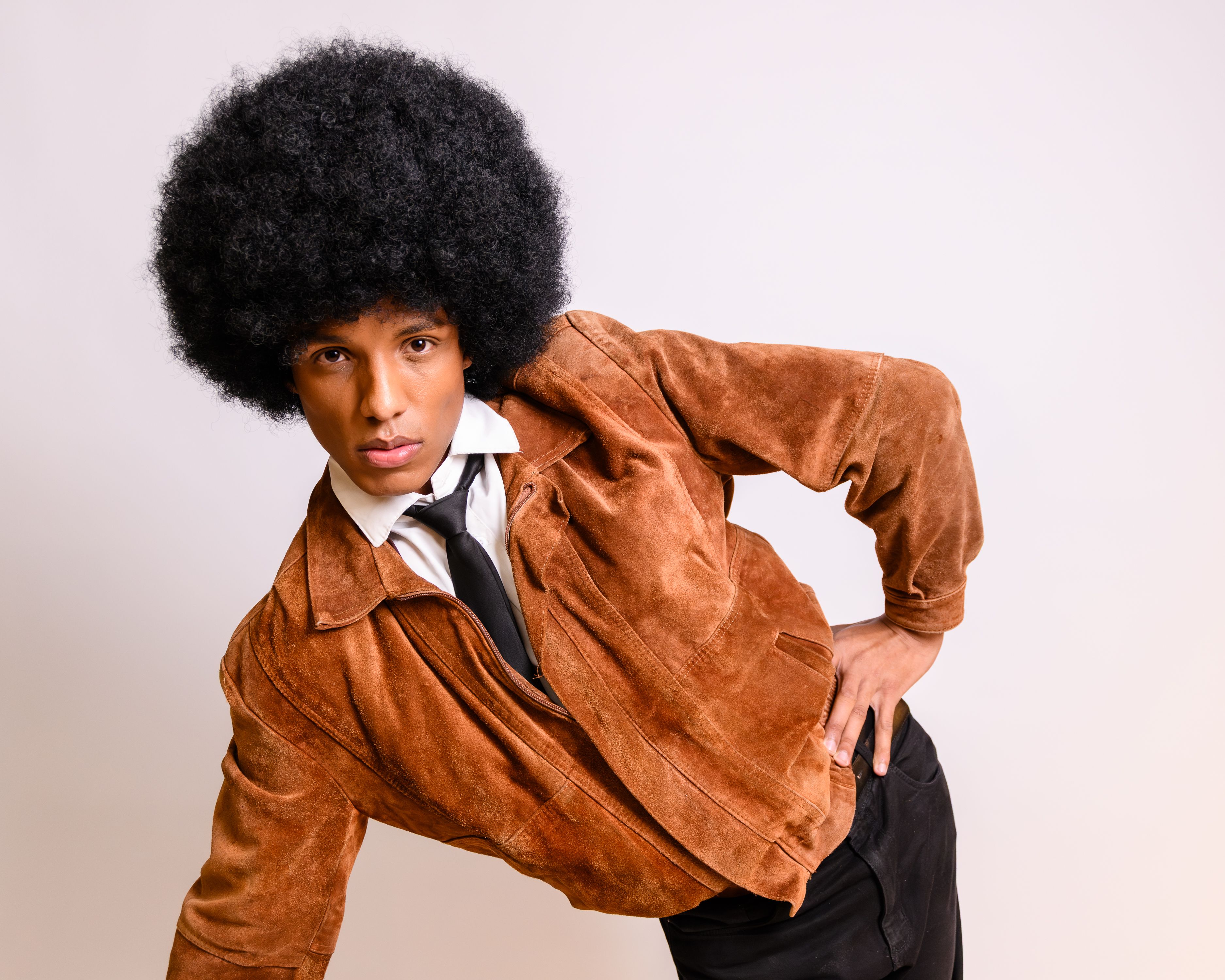 A fashionable man poses with a classic Afro hairstyle, wearing a vintage brown jacket.