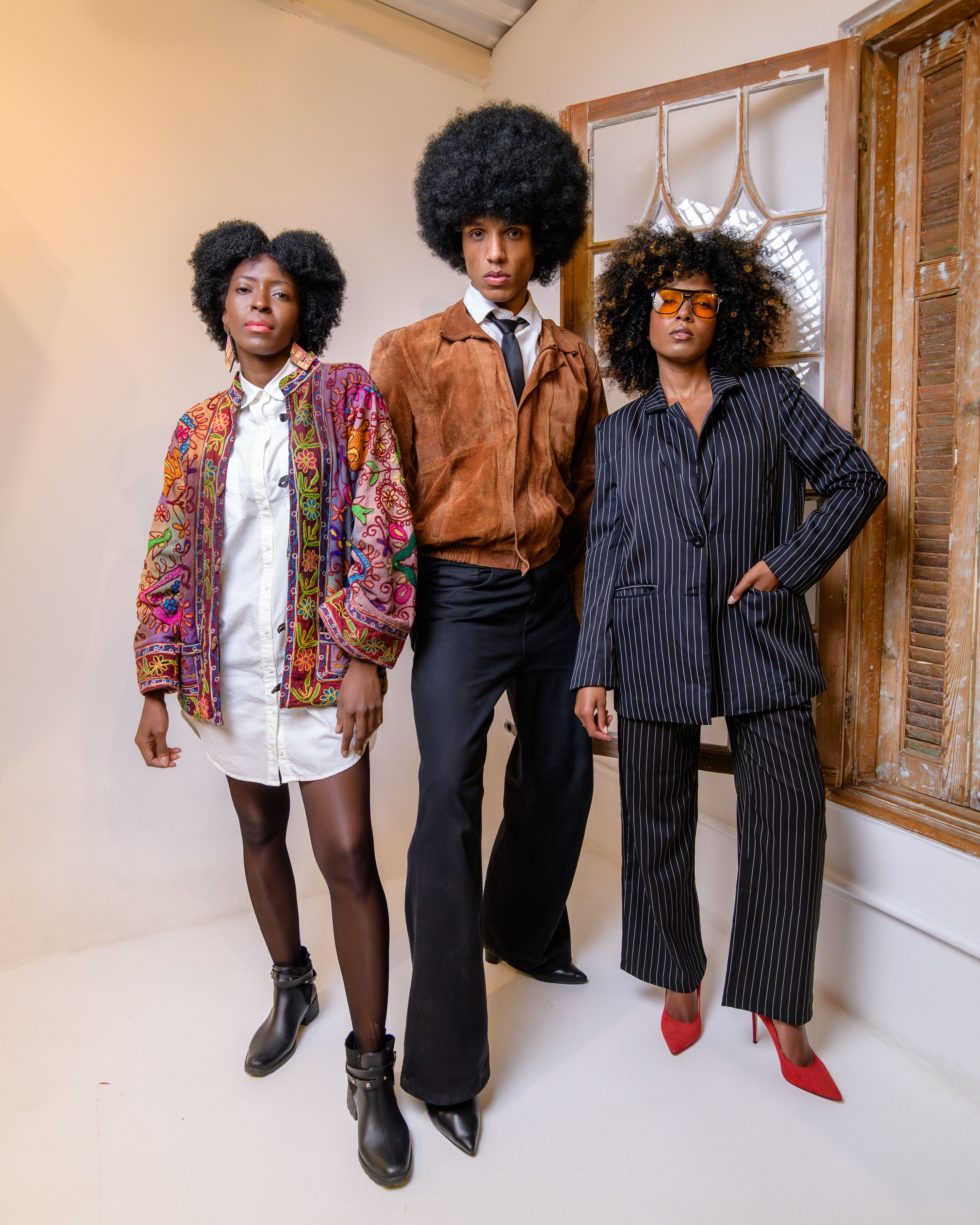 Fotomural Tres adultos con atuendos retro y peinados afro posan con estilo en interiores, reflejando la estética de la moda vintage.