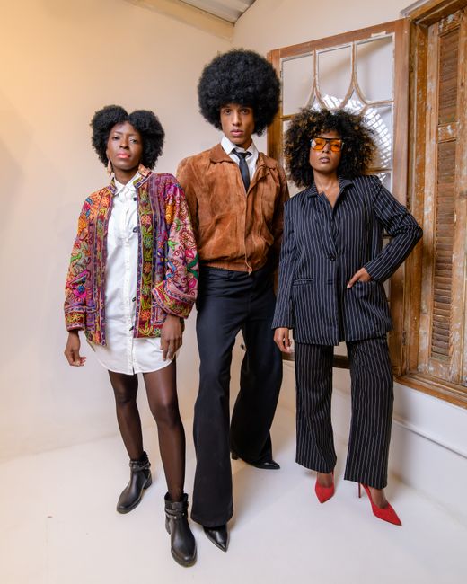 Fotomural Tres adultos con atuendos retro y peinados afro posan con estilo en interiores, reflejando la estética de la moda vintage.