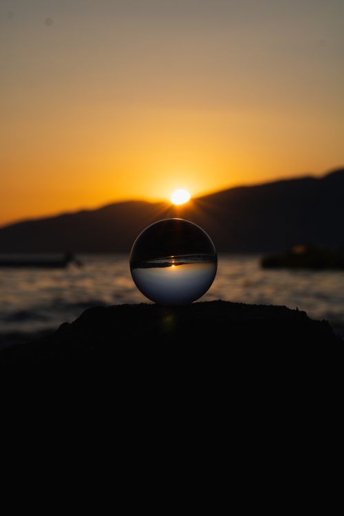 Free A captivating sunset reflected through a glass ball by the sea. Stock Photo