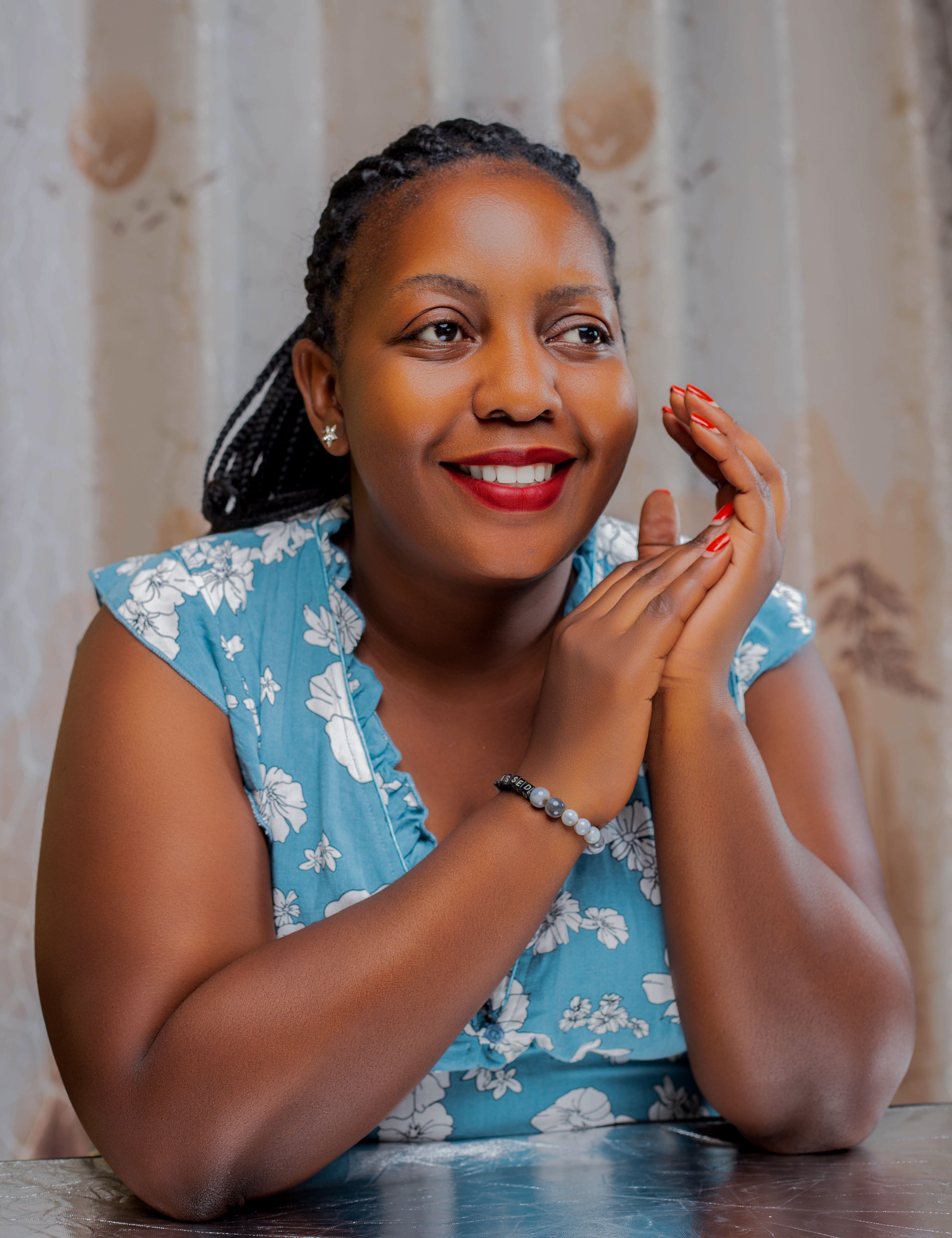 A cheerful woman in a blue floral dress smiles warmly indoors, exuding a sense of joy and positivity.