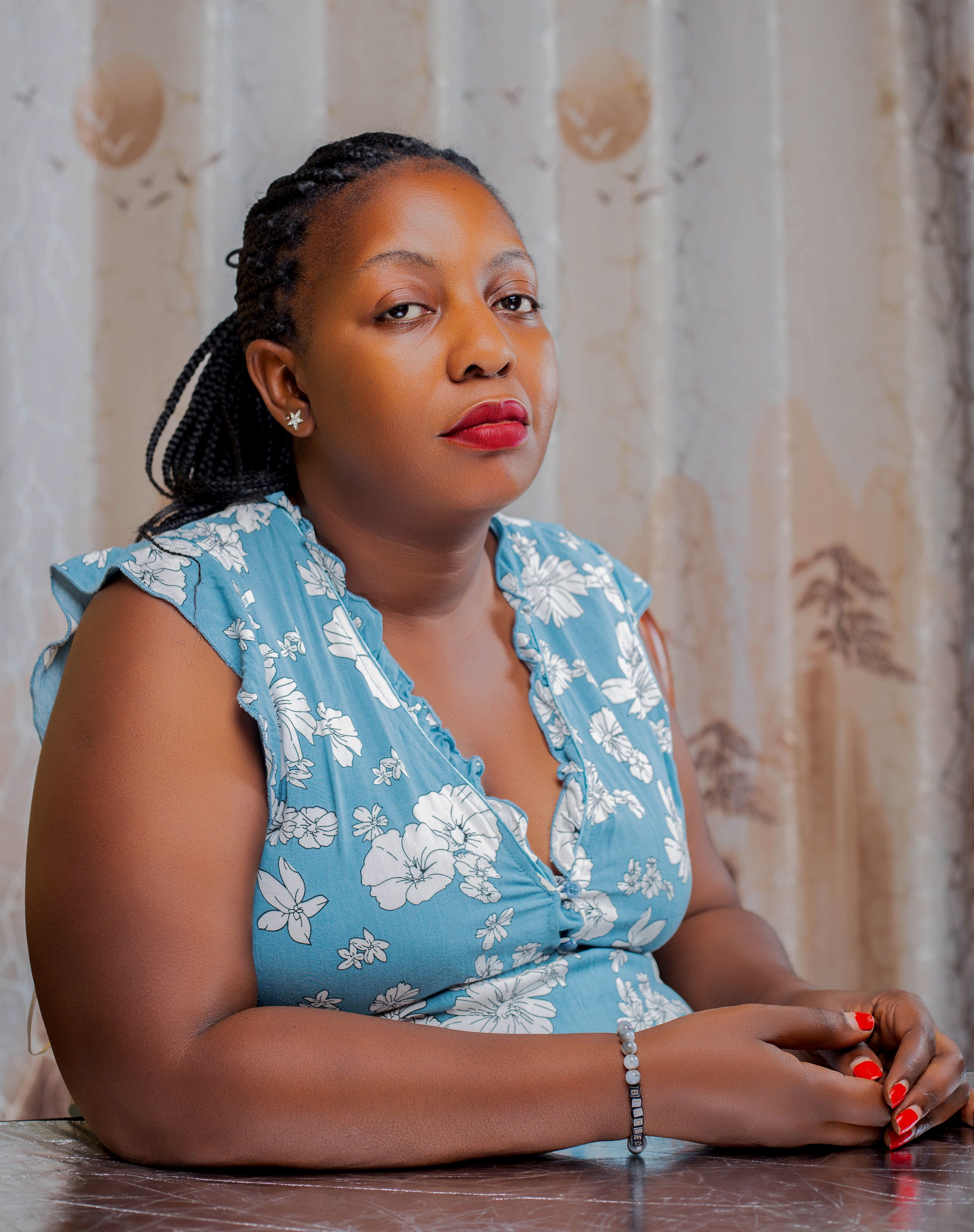 Portrait of a confident woman in a blue floral dress sitting indoors with a serene expression.
