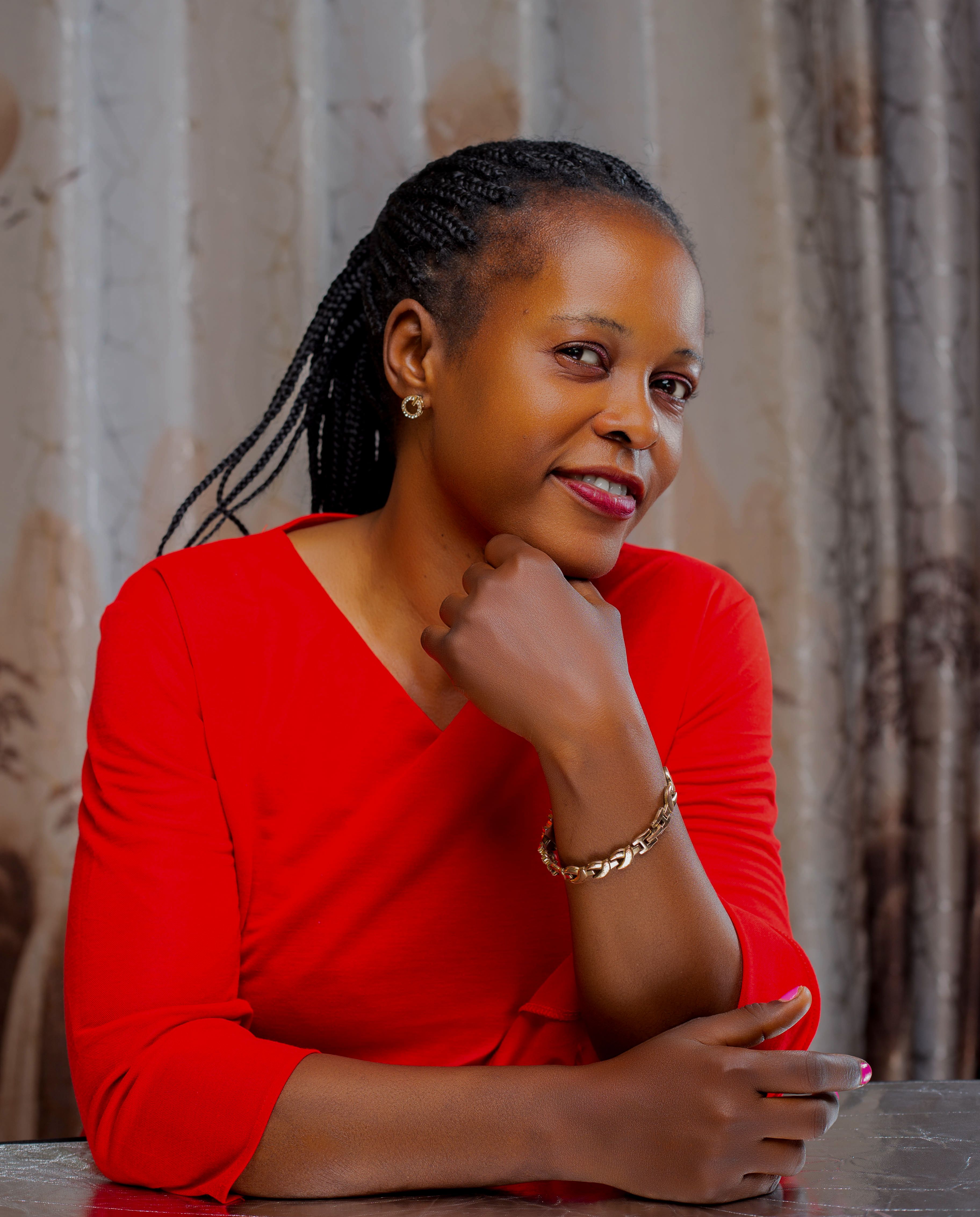 Confident woman wearing a red dress posing indoors with a thoughtful look.