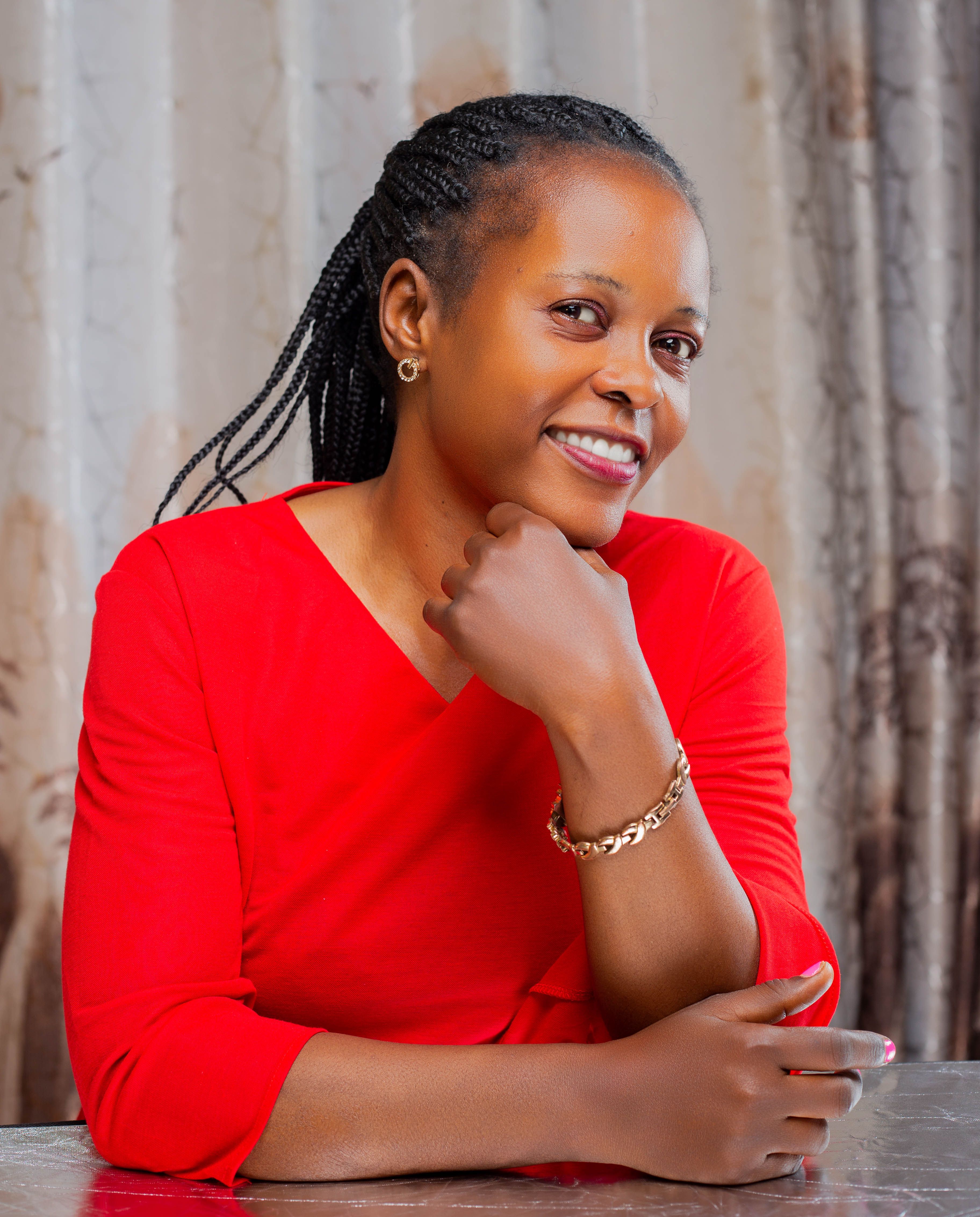 Portrait of a smiling woman in a red dress with braided hair, posing indoors.