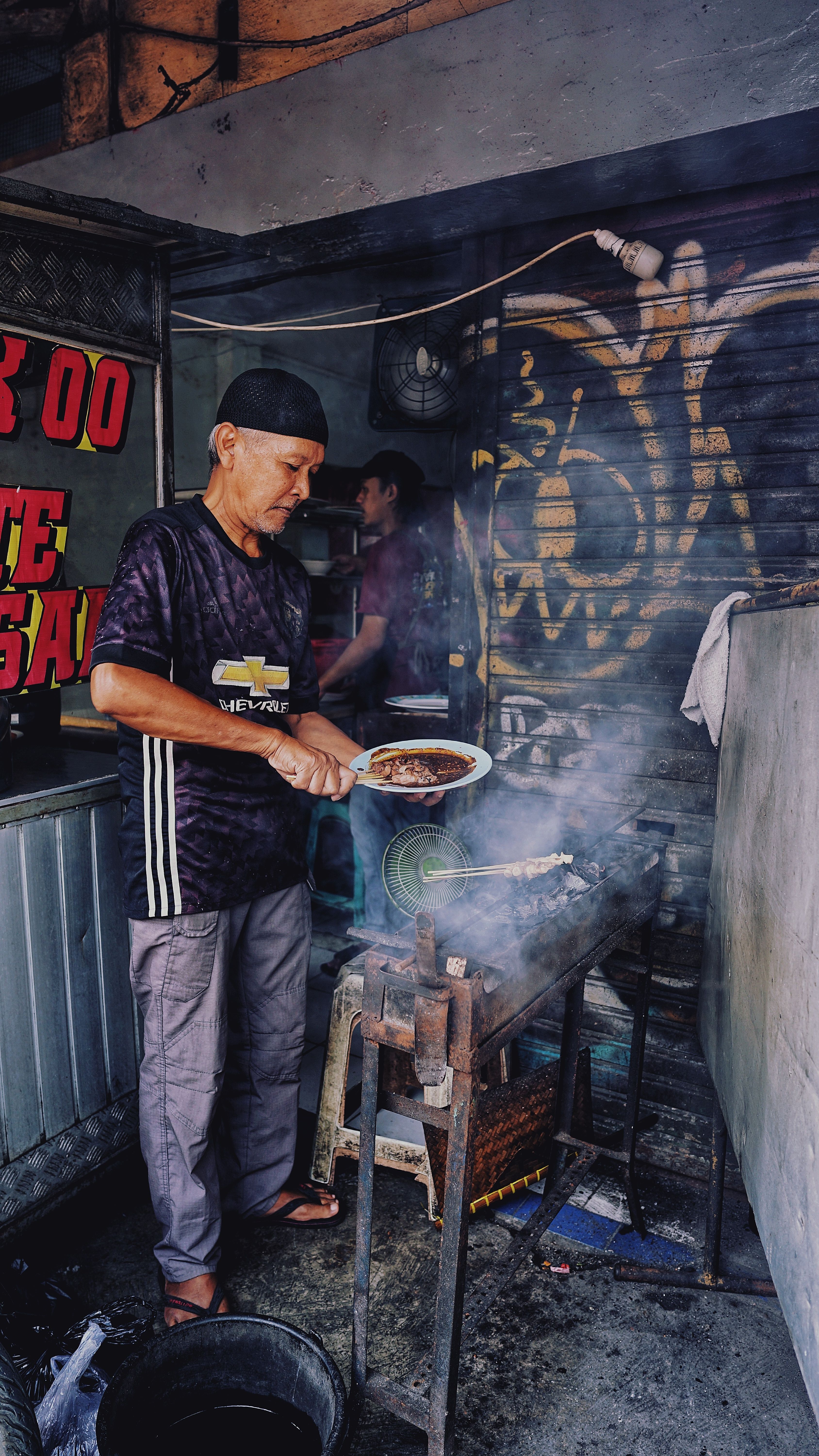 Street vendor cooking tasty grilled meat in traditional Jakarta food stall.