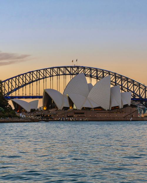 Free Iconic view of Sydney Opera House and Harbour Bridge during sunset, capturing Australia's distinctive skyline. Stock Photo