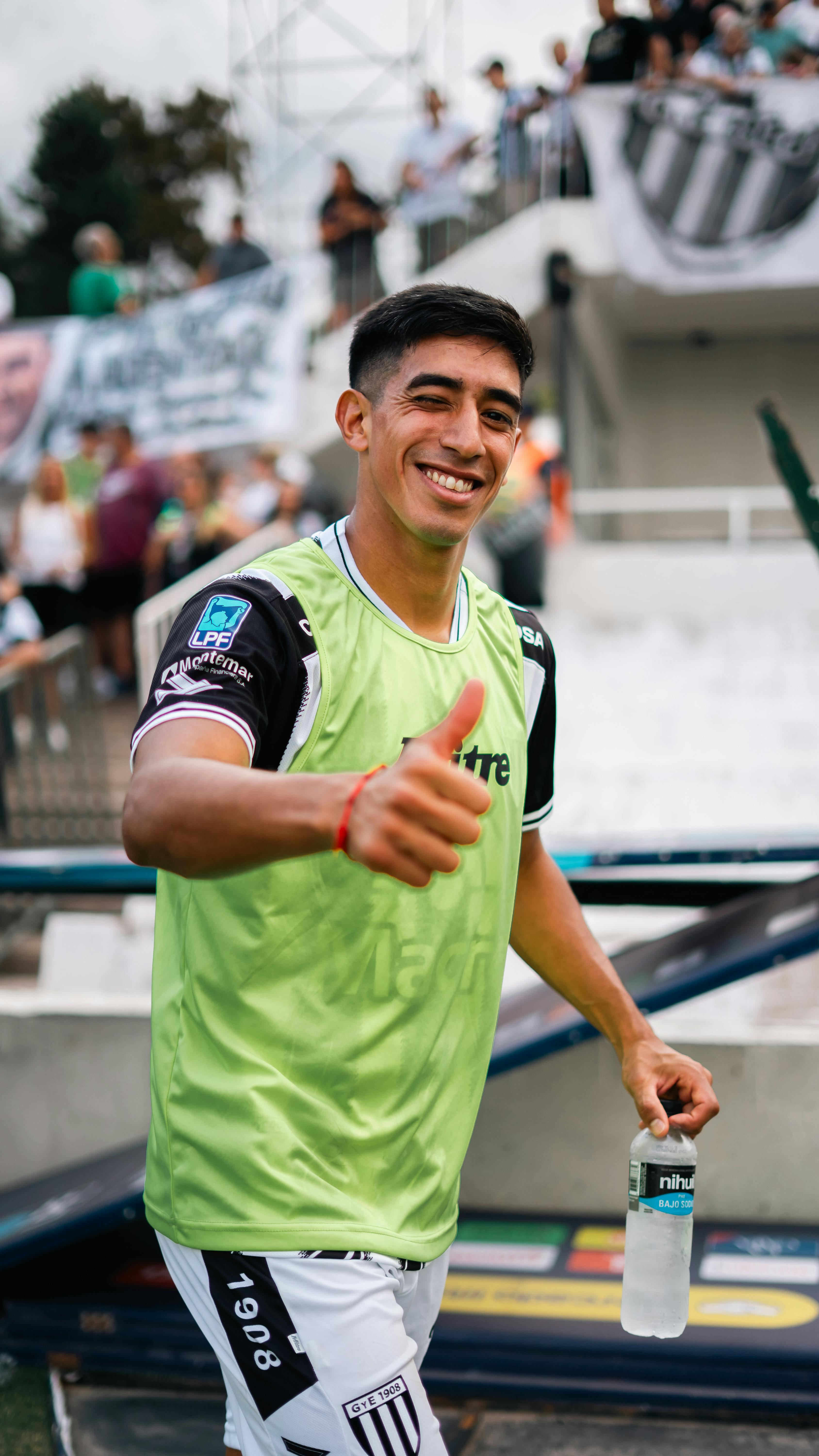 Smiling soccer player in green jersey giving thumbs up at a game.