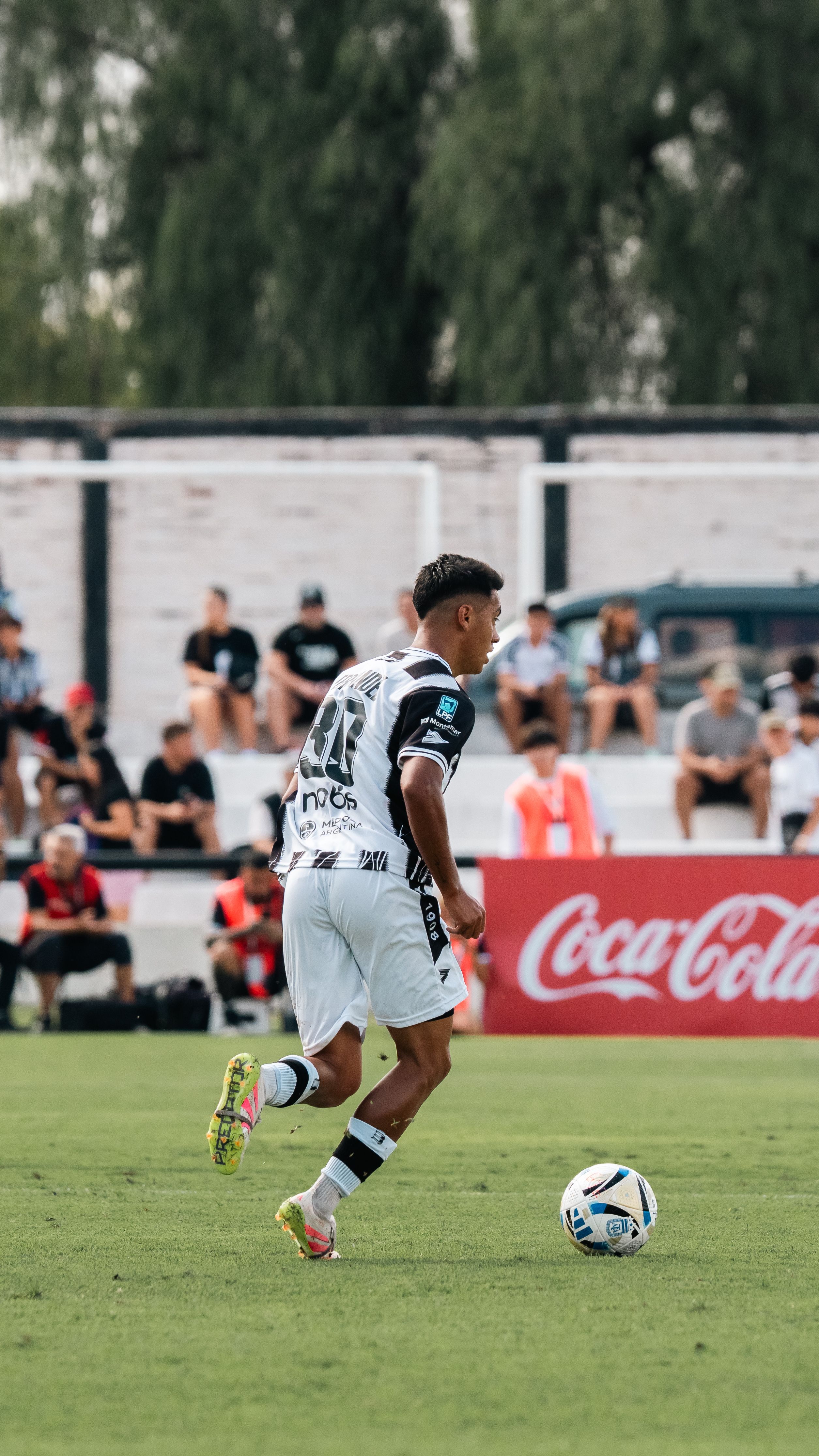 A soccer player in black and white jersey dribbles the ball on a green field during a match.
