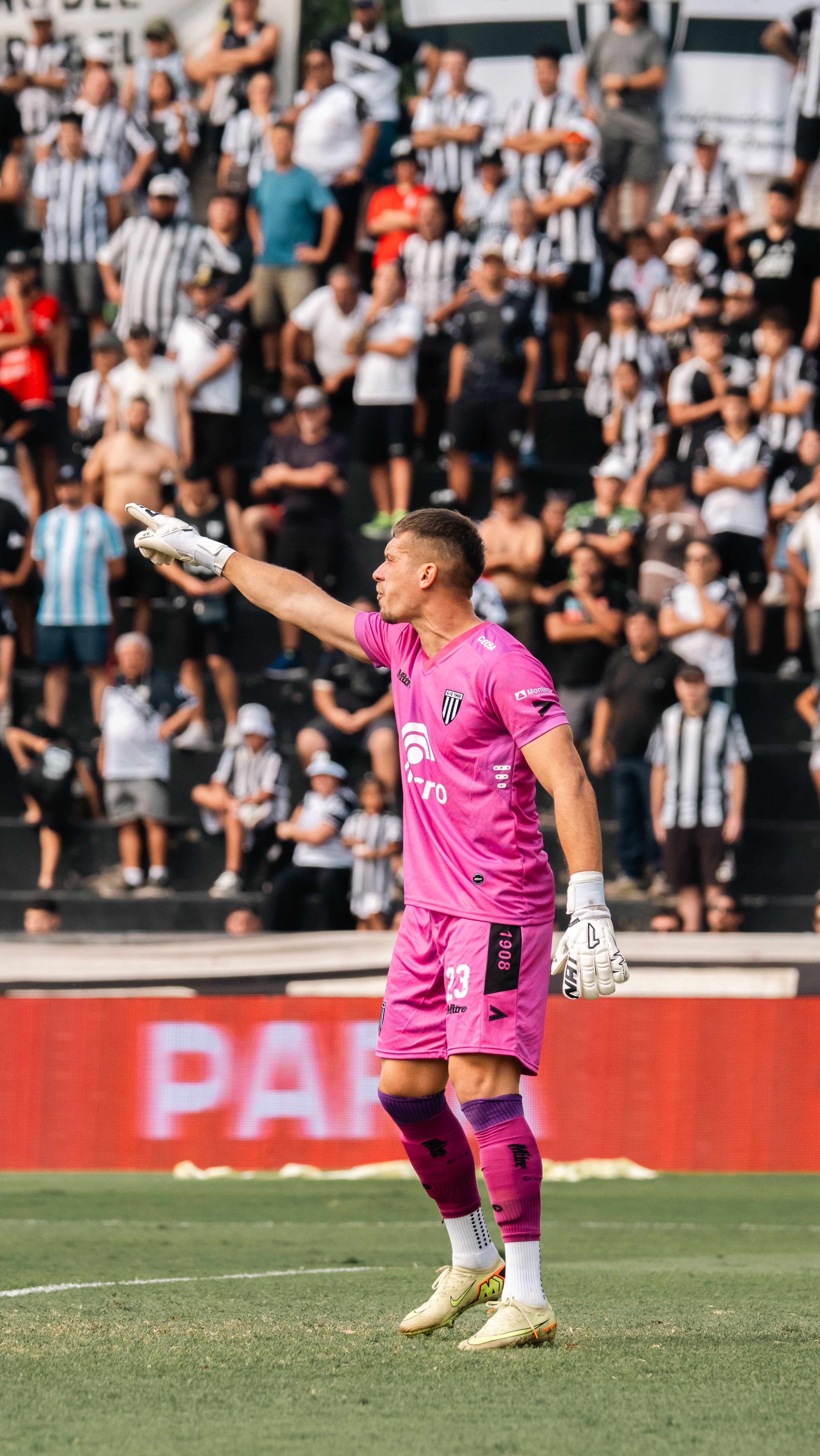 Goalkeeper directs teammates in a crowded soccer stadium setting.
