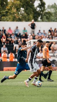 Players engaged in a competitive soccer match on a sunny day with an audience in the background.