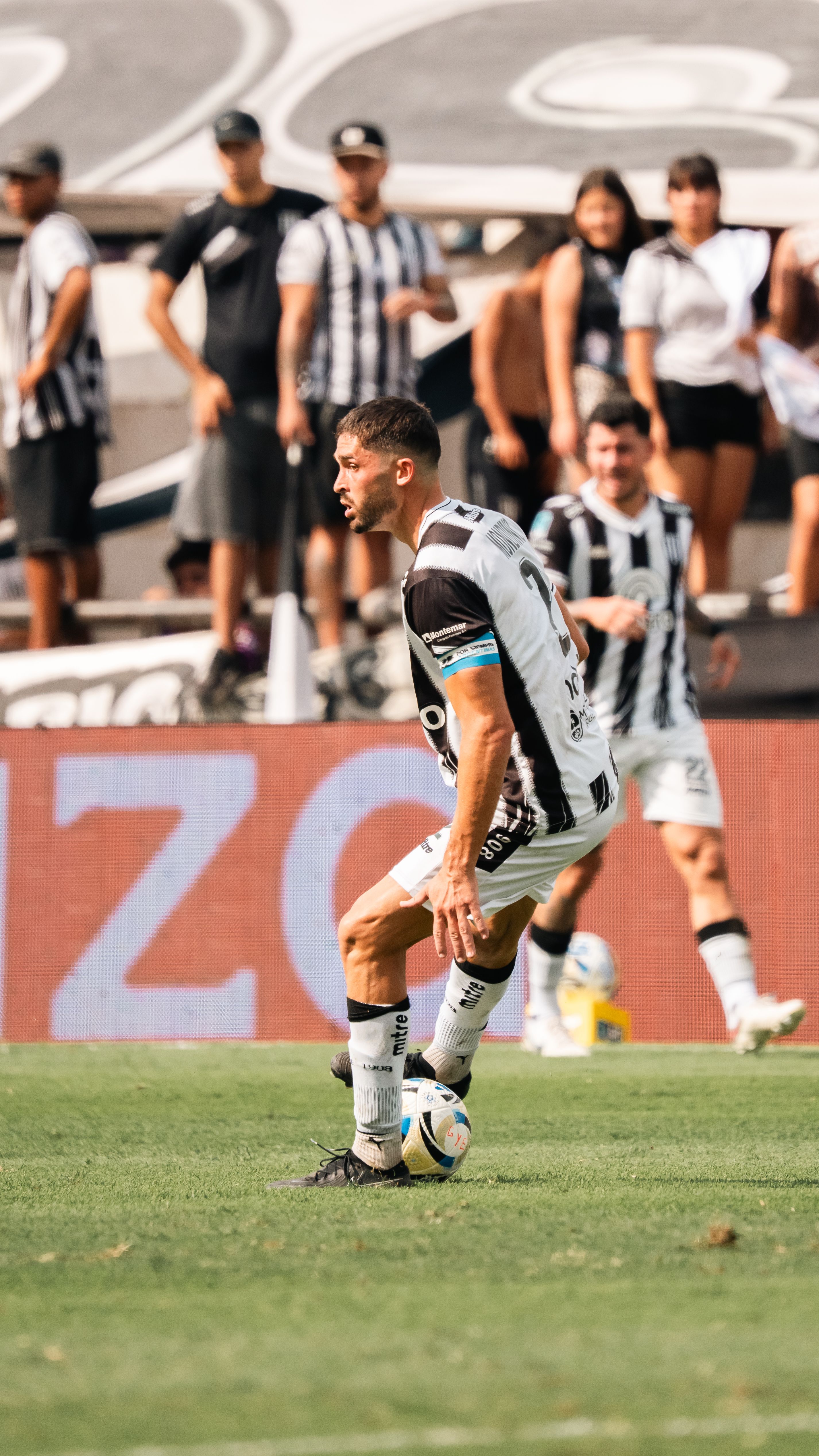 Athlete in black and white striped jersey dribbling during a soccer match in stadium.
