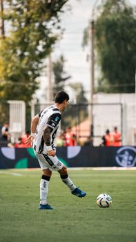 A soccer player in a black and white uniform kicks a ball during a daytime match.