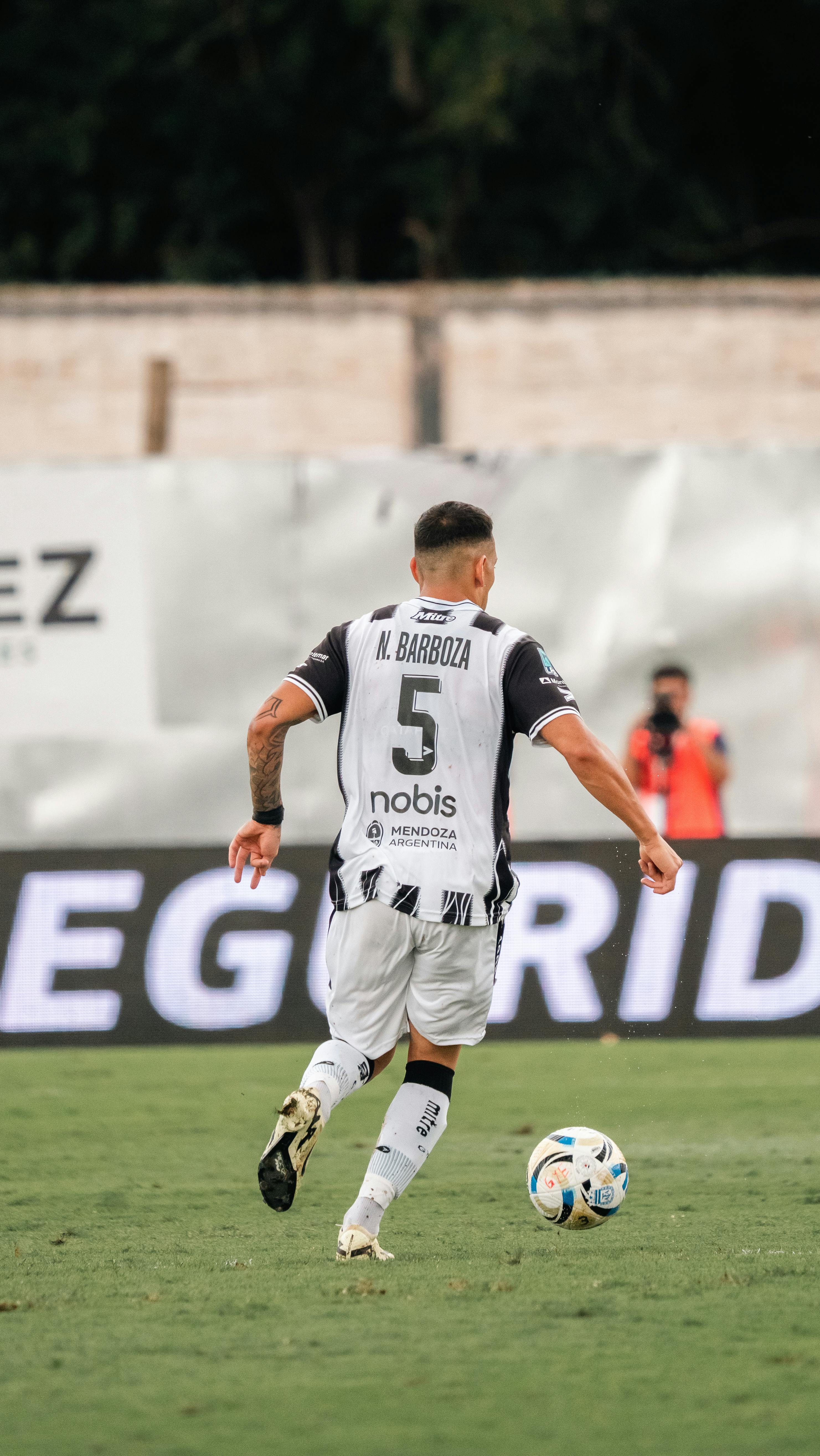 Soccer player with jersey number five controls the ball during a match outdoors.